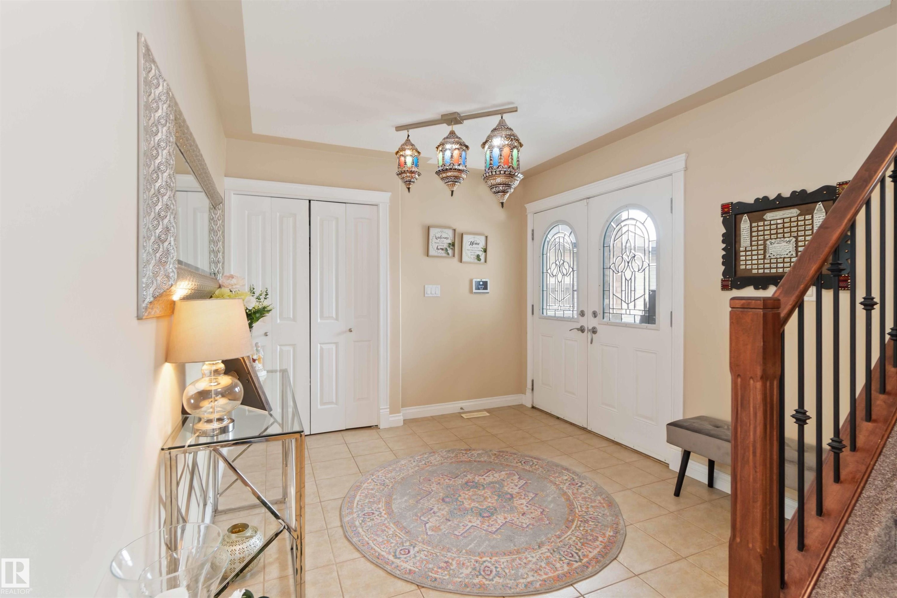 Entryway featuring double doors with decorative glass panels, tile flooring, a built-in closet, a wooden staircase with black iron balusters, and a unique multi-light fixture - 6116 53 Avenue, Beaumont, AB - Indoor Photo Showing Other Room