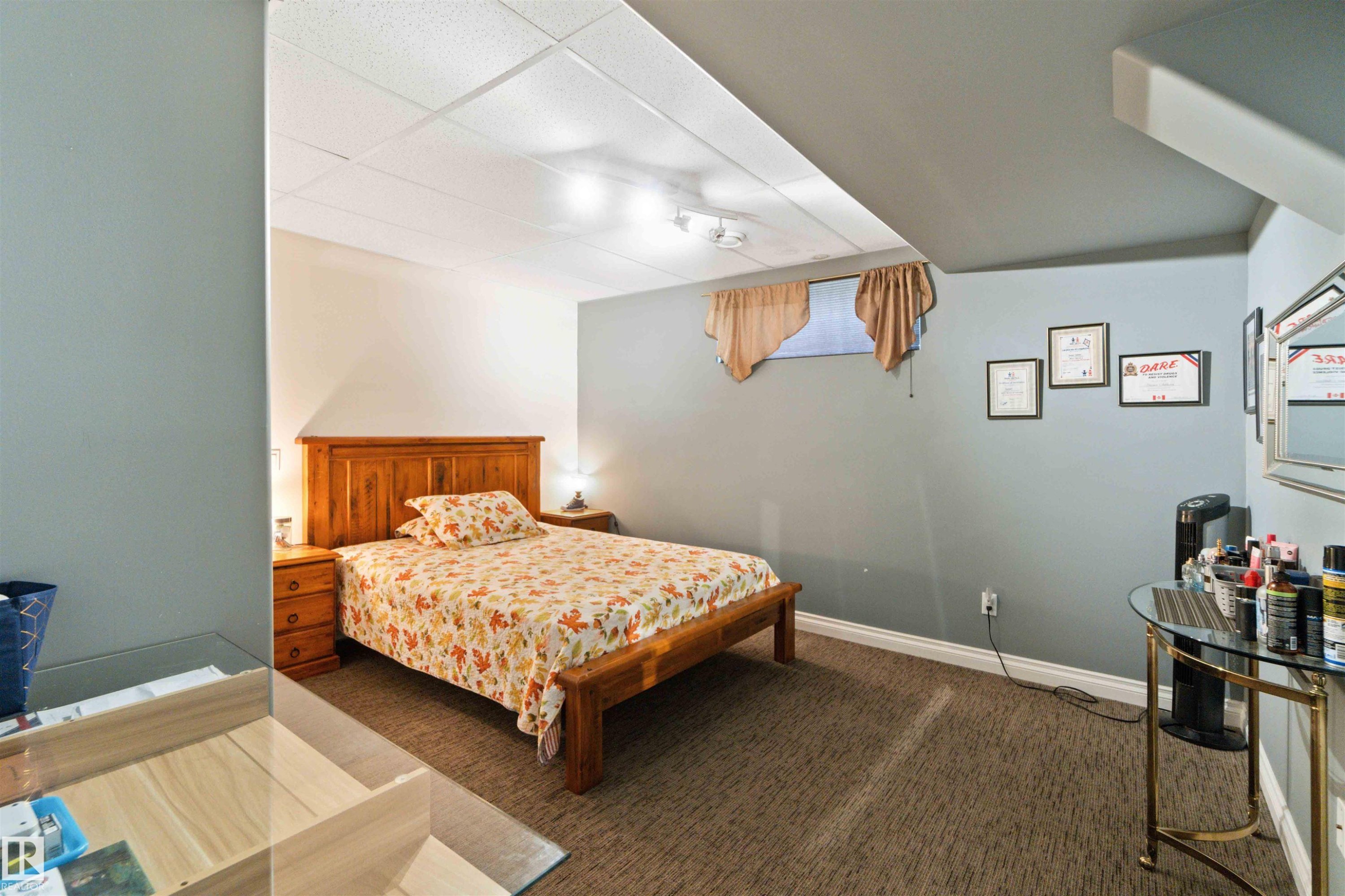 Carpeted bedroom featuring a wooden bed frame, two wooden nightstands with lamps, and a window with valances - 6116 53 Avenue, Beaumont, AB - Indoor Photo Showing Bedroom