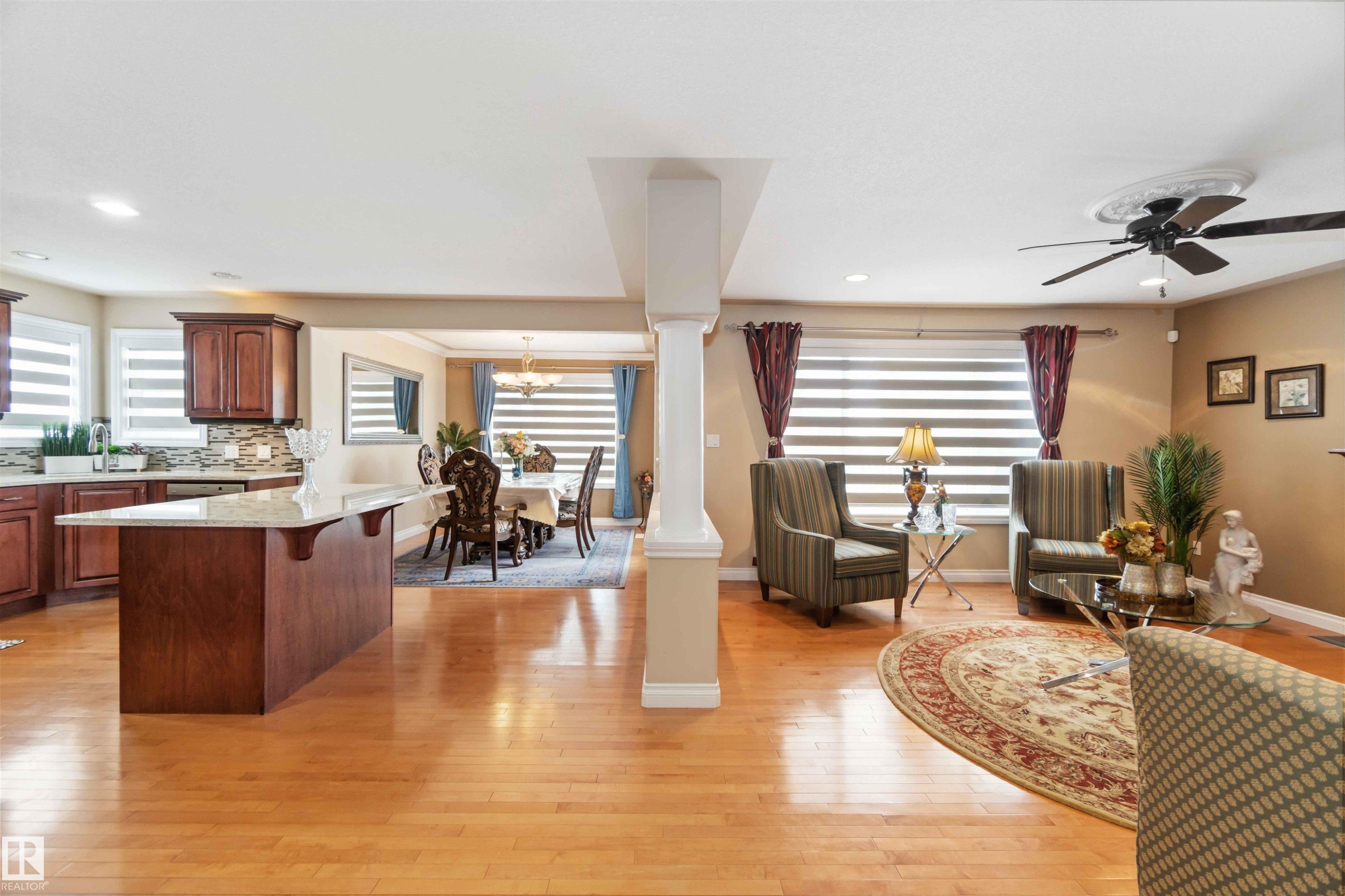 Hardwood flooring throughout featuring a kitchen island with stone countertop, wood cabinetry, and a tile backsplash - 6116 53 Avenue, Beaumont, AB - Indoor