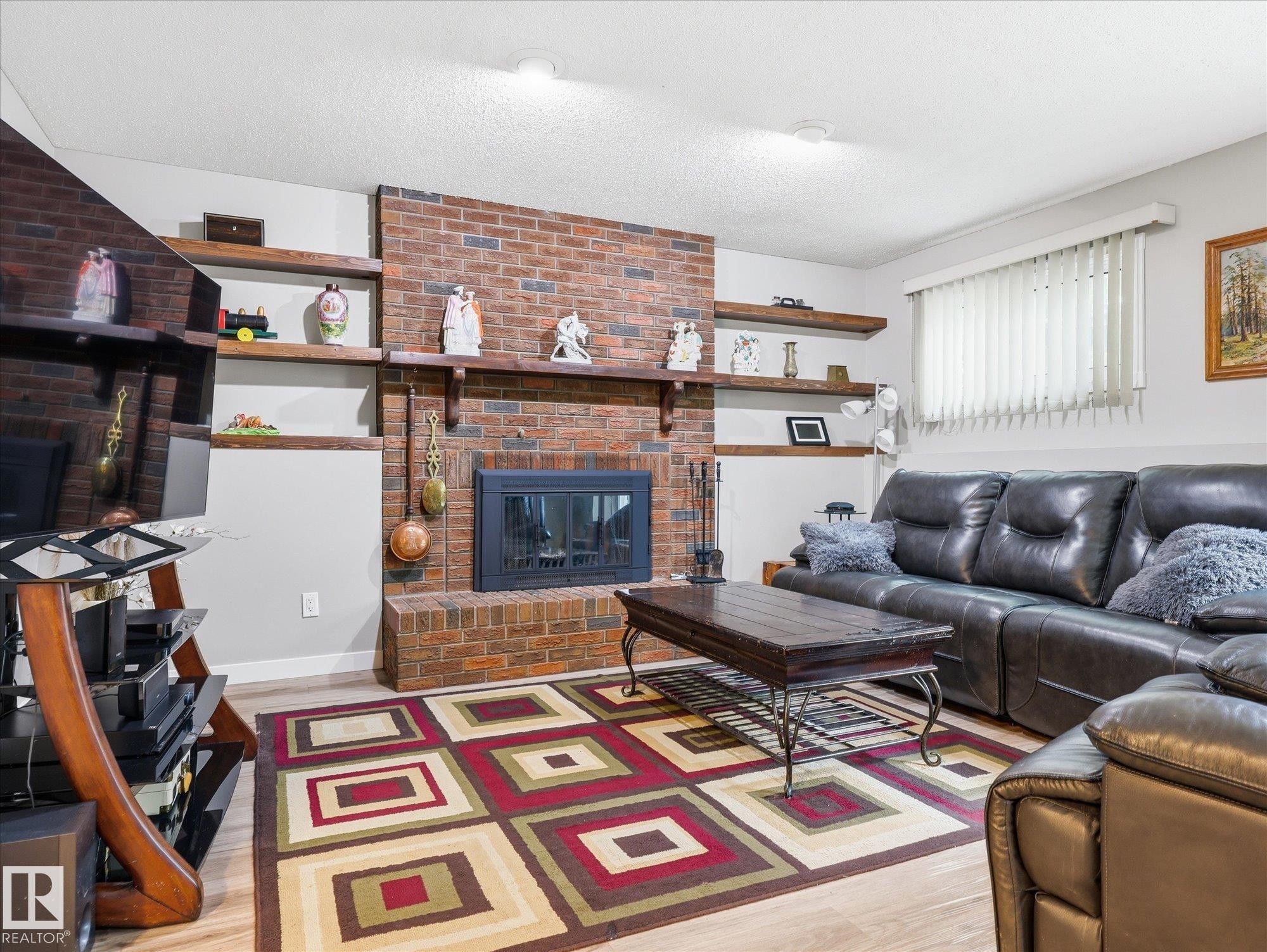 Brick fireplace with an integrated firebox, flanked by built-in shelving and light wood-finish flooring - 18627 62A Avenue, Edmonton, AB - Indoor Photo Showing Living Room With Fireplace