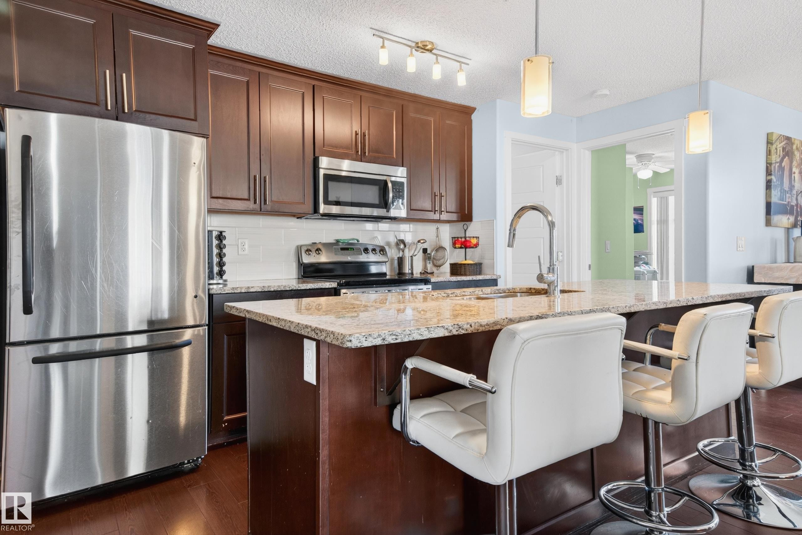 Kitchen featuring dark wood cabinetry, stainless steel appliances, and a light-toned granite countertop - 340 6076 Schonsee Way, Edmonton, AB - Indoor Photo Showing Kitchen With Stainless Steel Kitchen With Upgraded Kitchen