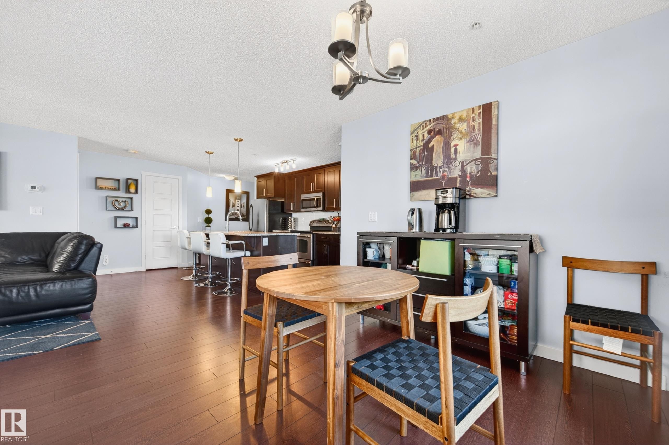 Open-concept living space featuring wood-finish flooring, a kitchen island with pendant lighting, and a defined dining area - 340 6076 Schonsee Way, Edmonton, AB - Indoor