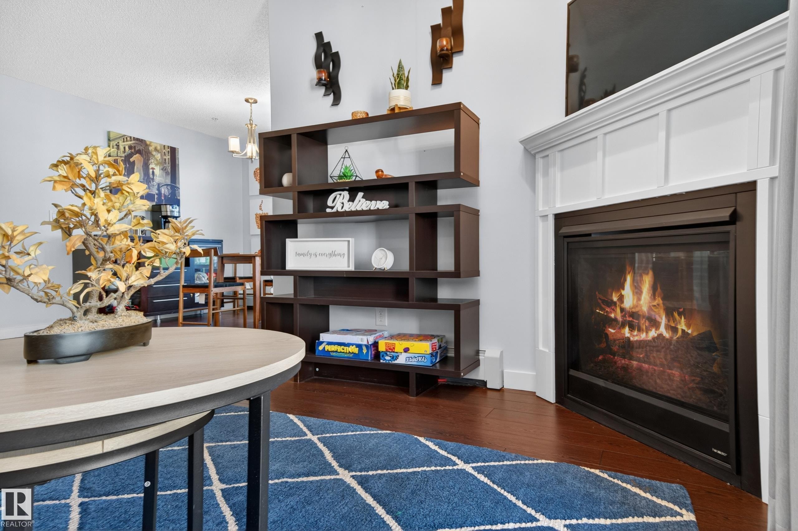 Living area featuring a corner-mounted fireplace with white paneled surround, dark wood-finish flooring, and light wall tones - 340 6076 Schonsee Way, Edmonton, AB - Indoor With Fireplace