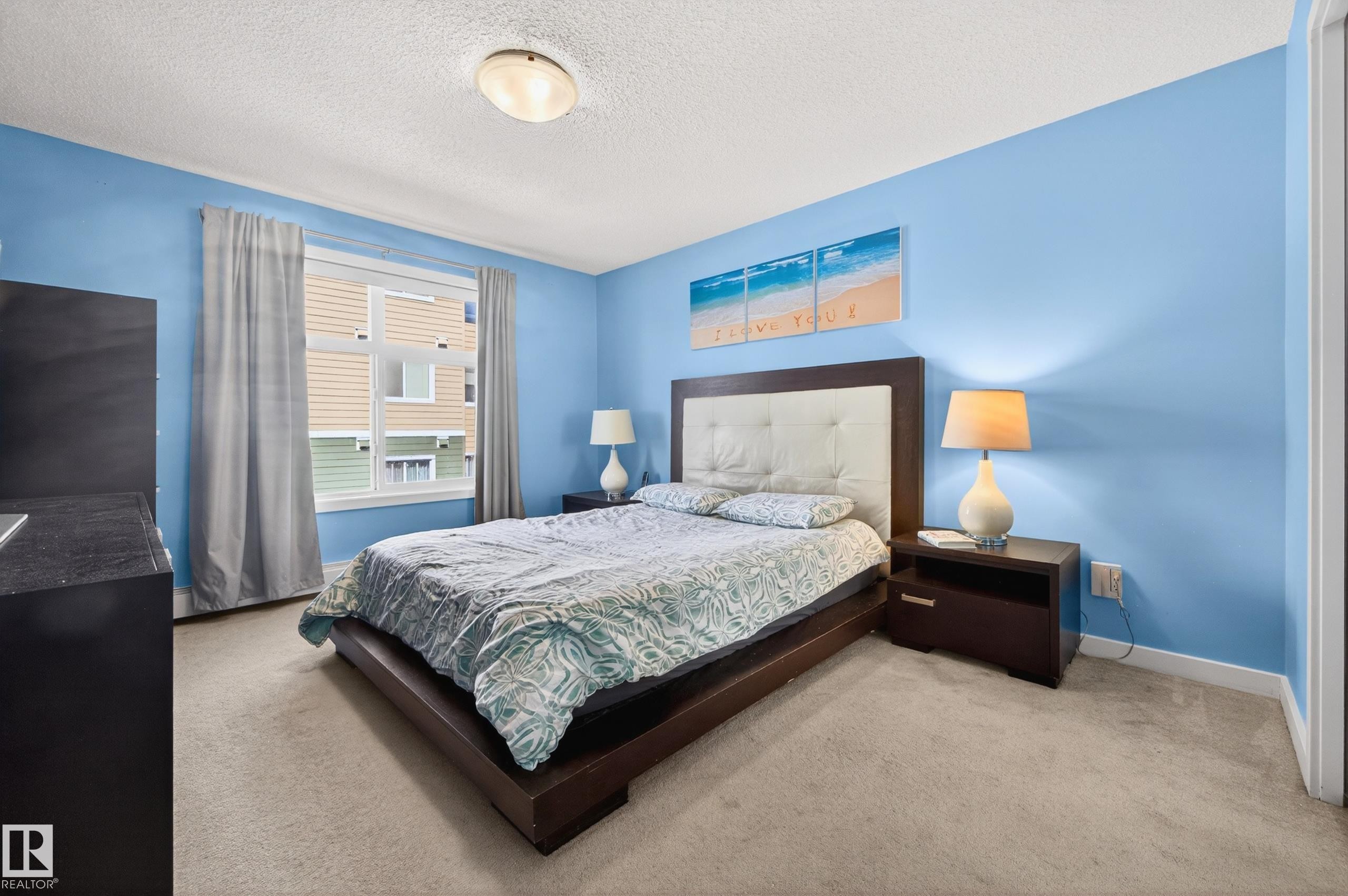 Carpeted room with a ceiling-mounted light fixture, light blue walls, and a window with curtains - 340 6076 Schonsee Way, Edmonton, AB - Indoor Photo Showing Bedroom