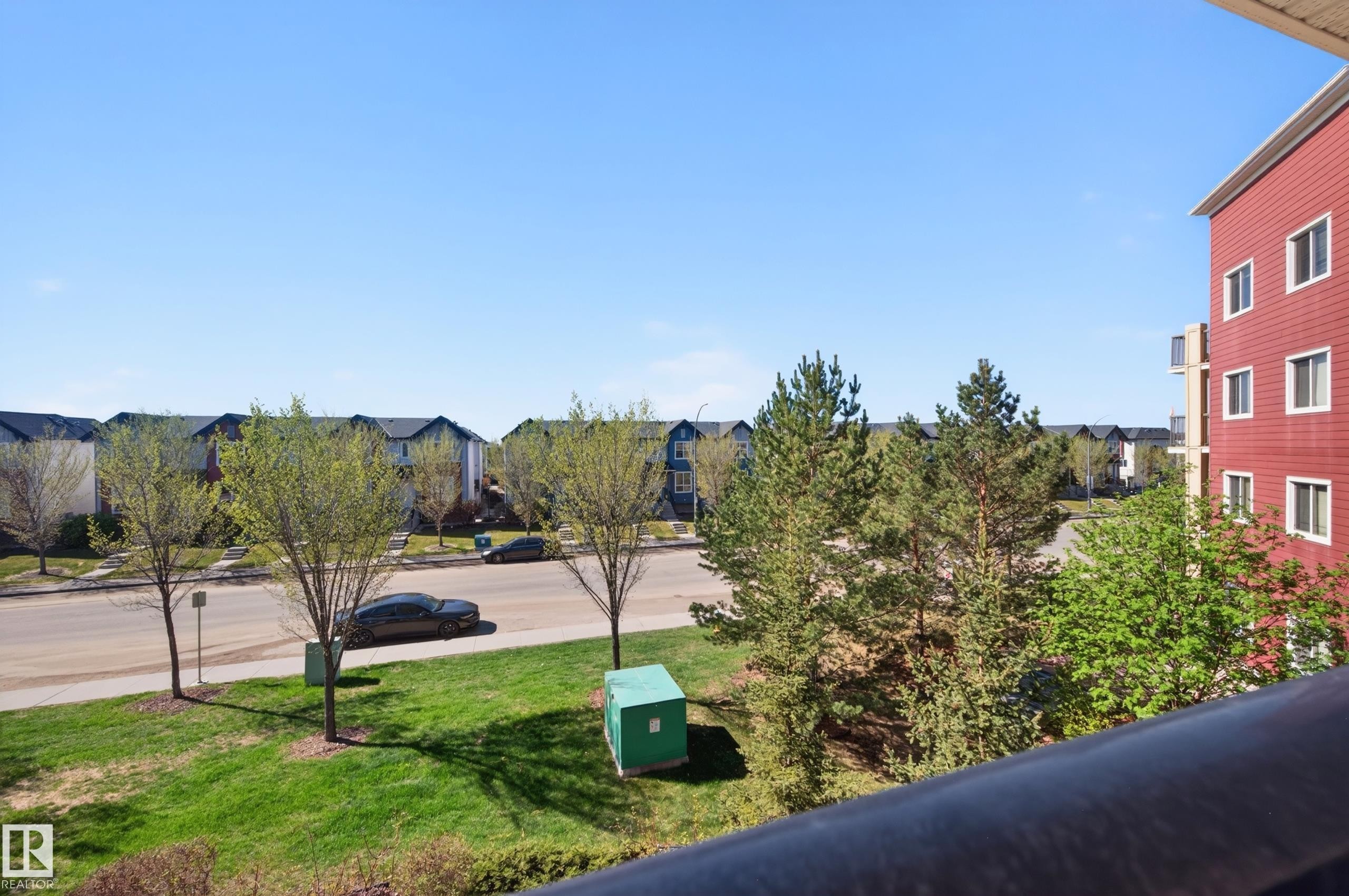 Street scene featuring a paved road, green lawns, and a variety of trees - 340 6076 Schonsee Way, Edmonton, AB - Outdoor