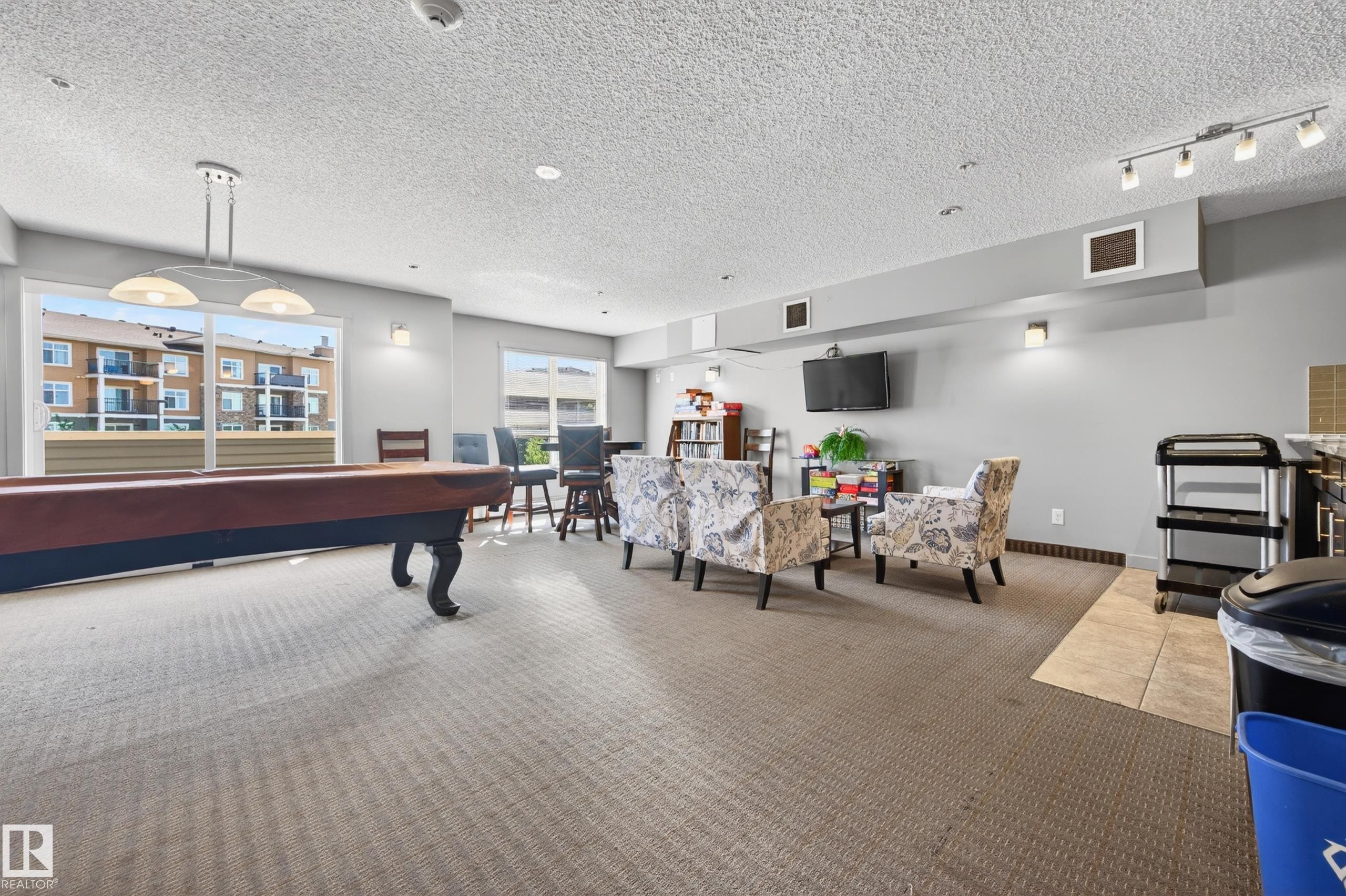 Spacious common area featuring a billiard table, extensive carpeting, large windows, and track lighting - 340 6076 Schonsee Way, Edmonton, AB - Indoor