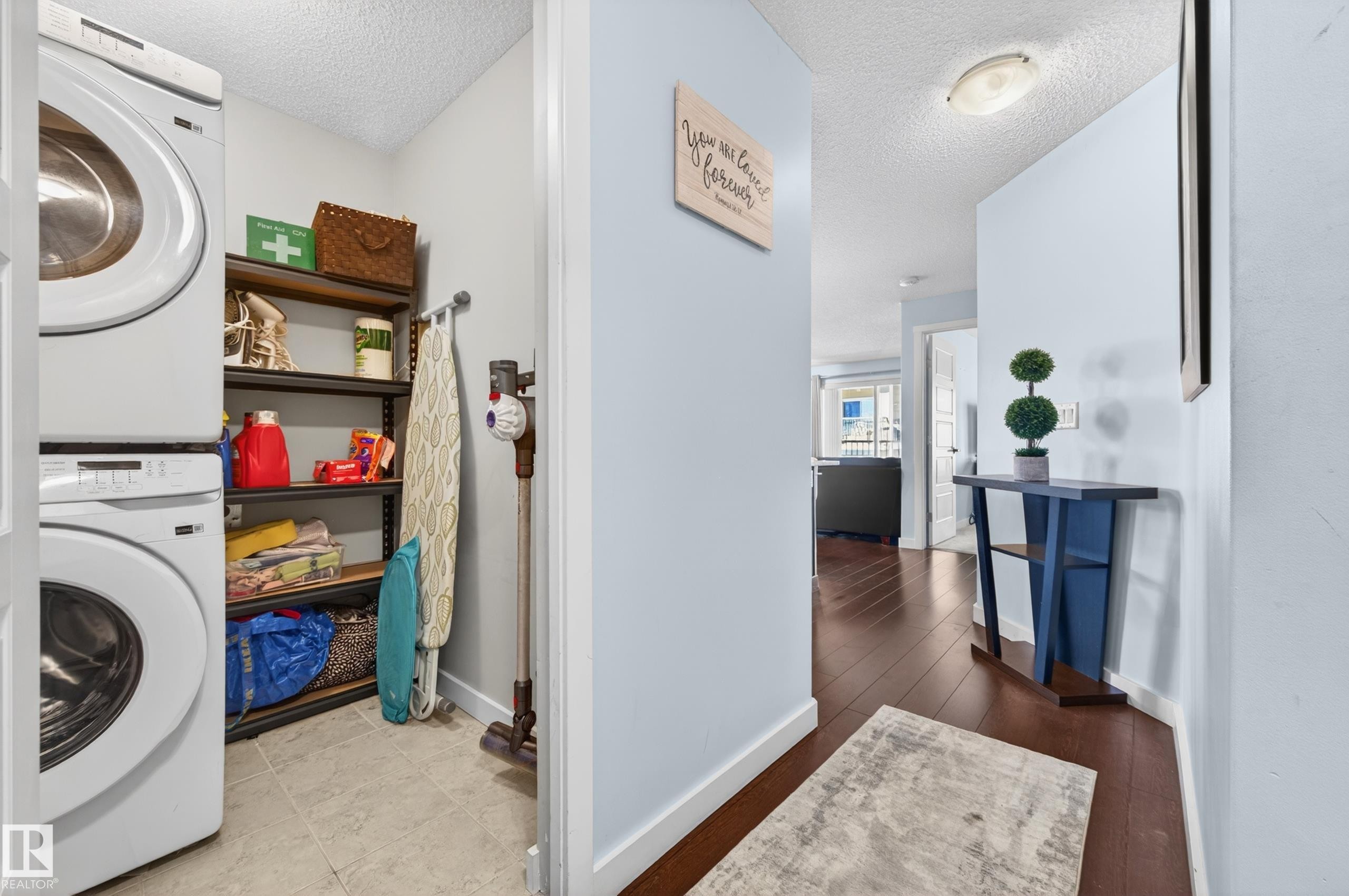 Dedicated laundry area featuring stacked appliances and shelving - 340 6076 Schonsee Way, Edmonton, AB - Indoor Photo Showing Laundry Room