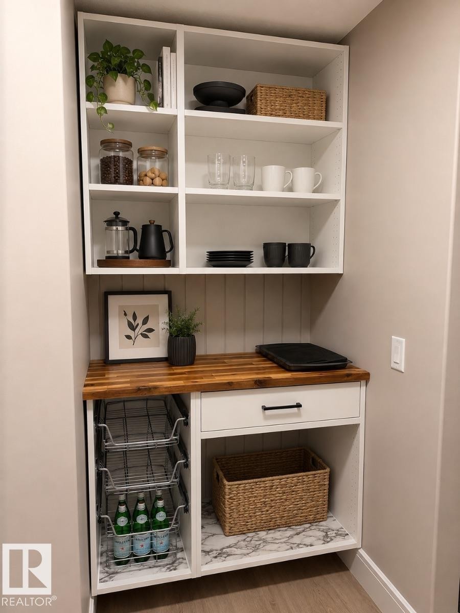 Built-in white cabinetry with a wood-finish countertop, open shelving, a white drawer with a matte black pull, and lower storage with a marble-patterned base - 648 178 Street, Edmonton, AB