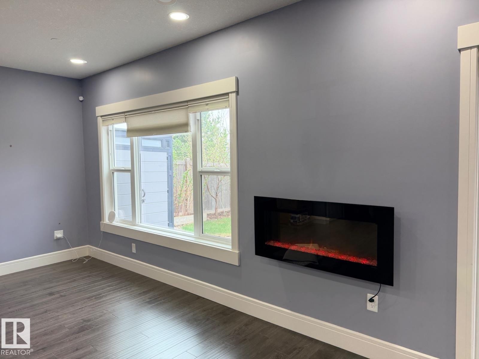 Spacious interior featuring a wall-mounted electric fireplace, recessed ceiling lighting, light blue walls, dark wood-finish flooring, and white trim - 648 178 Street, Edmonton, AB