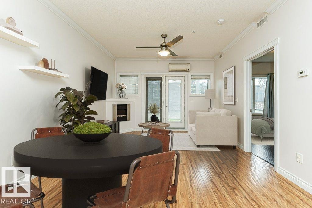 Open-concept living space with wood-finish flooring, crown molding, a built-in fireplace, and direct access to an outdoor area - #145 10121 80 Av Nw, Edmonton, AB - Indoor Photo Showing Dining Room