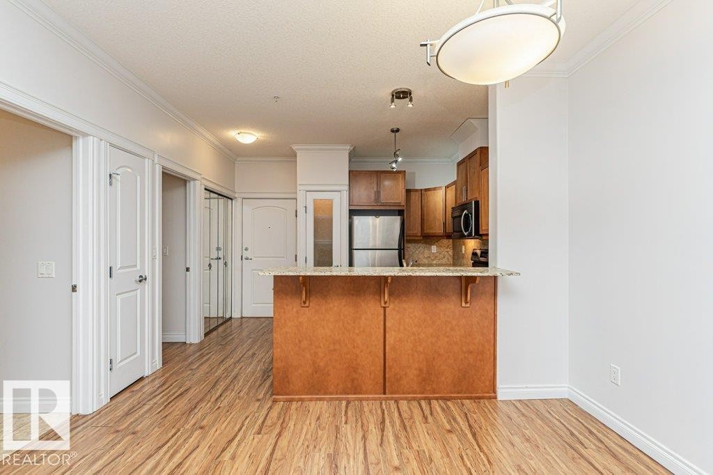Open-concept living area featuring wood-finish flooring, crown molding, and a kitchen island with a granite countertop - #145 10121 80 Av Nw, Edmonton, AB - Indoor Photo Showing Kitchen