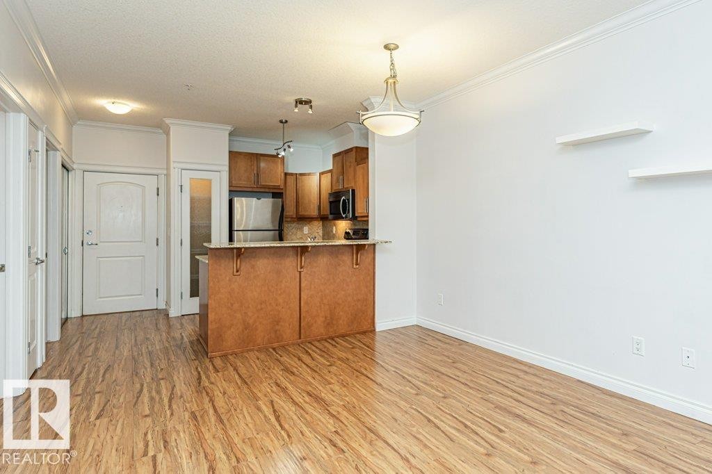 Open-concept living area featuring wood-finish flooring, crown molding, and a kitchen island with seating - #145 10121 80 Av Nw, Edmonton, AB - Indoor Photo Showing Kitchen