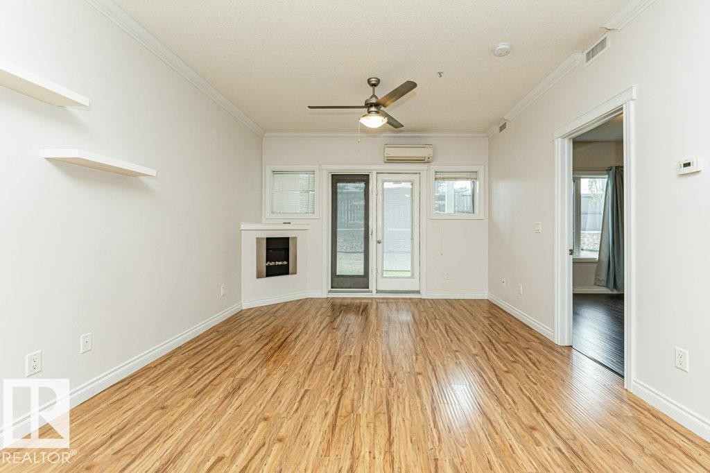Spacious room featuring wood-finish flooring, a built-in fireplace, a glass-paned exterior door, and a ceiling fan with integrated lighting - #145 10121 80 Av Nw, Edmonton, AB - Indoor Photo Showing Other Room