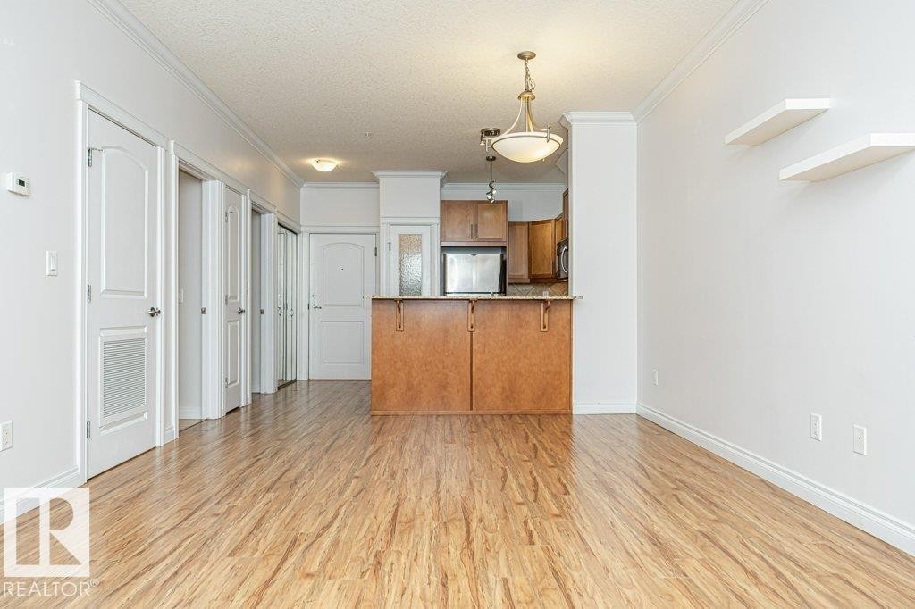 Open-concept living space featuring wood-finish flooring, white walls, and crown molding - #145 10121 80 Av Nw, Edmonton, AB - Indoor