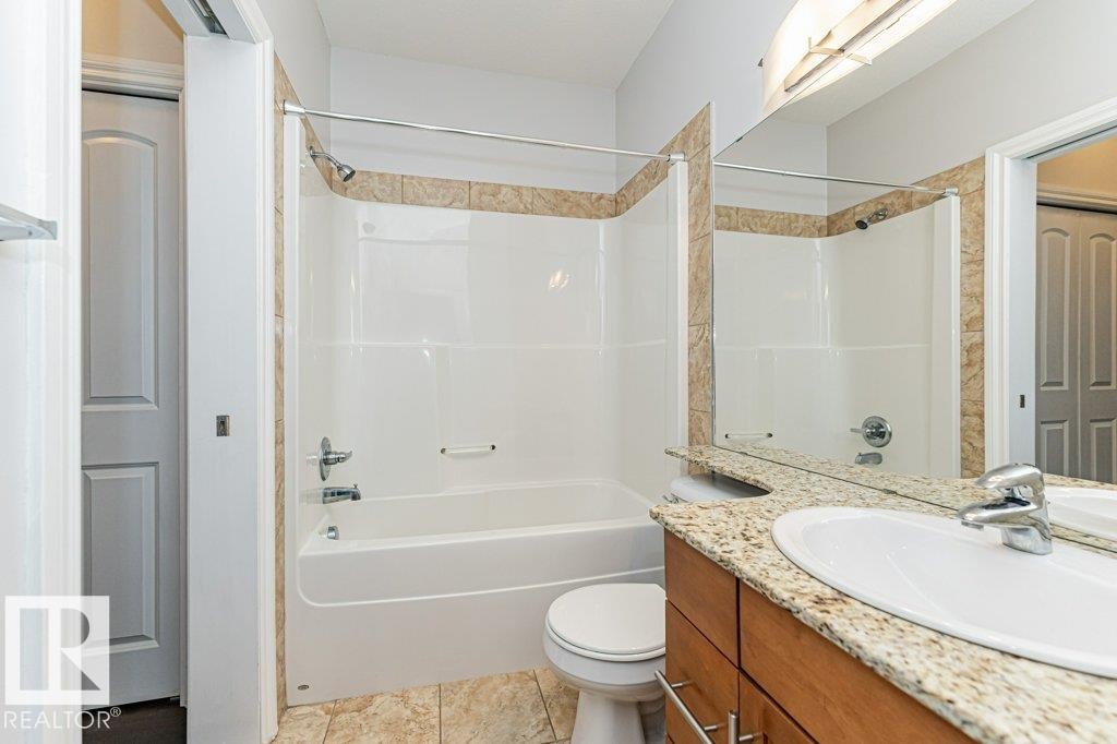 Bathroom featuring a tub and shower combination with tiled surround, a vanity with a light-toned countertop, and wood-finish cabinetry - #145 10121 80 Av Nw, Edmonton, AB - Indoor Photo Showing Bathroom