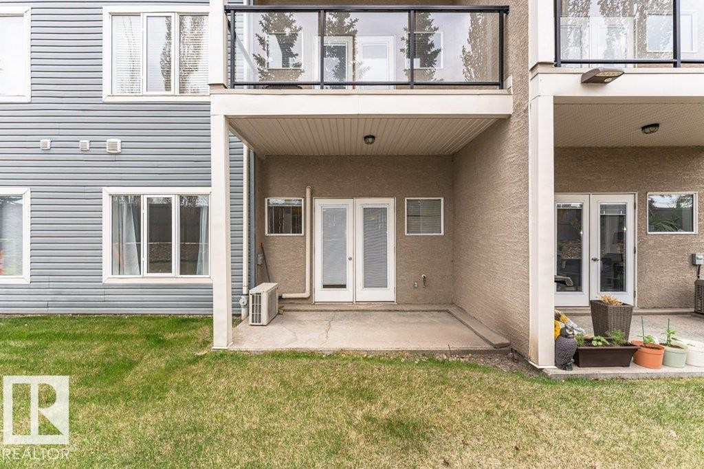 Ground-level concrete patio with covered overhead structure, dual glass panel doors, and exterior wall lighting - #145 10121 80 Av Nw, Edmonton, AB - Outdoor With Exterior