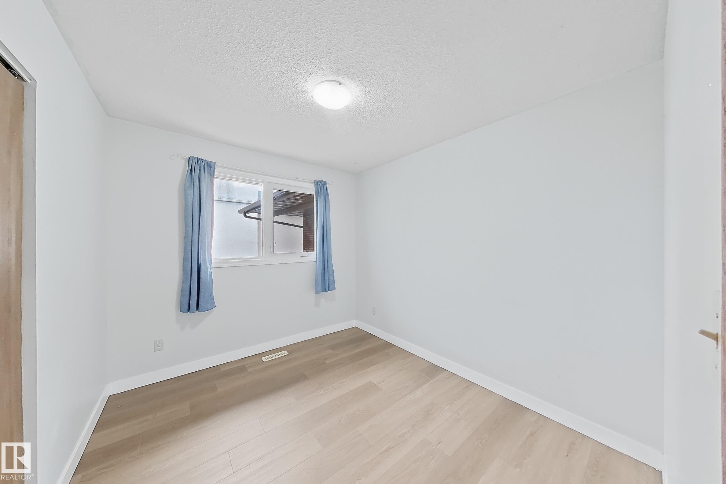 Room with light wood-finish flooring, white walls, and a window featuring light blue curtains - 1731 51 Street, Edmonton, AB - Indoor Photo Showing Other Room