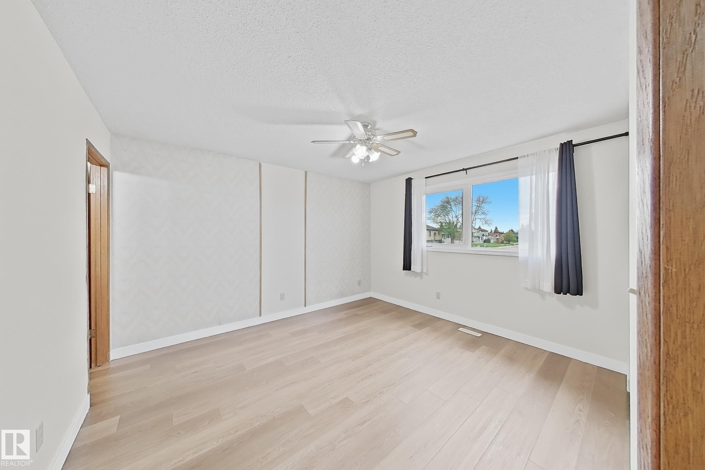 Spacious room featuring light wood-finish flooring, a ceiling fan with integrated lighting, and a large window - 1731 51 Street, Edmonton, AB - Indoor Photo Showing Other Room