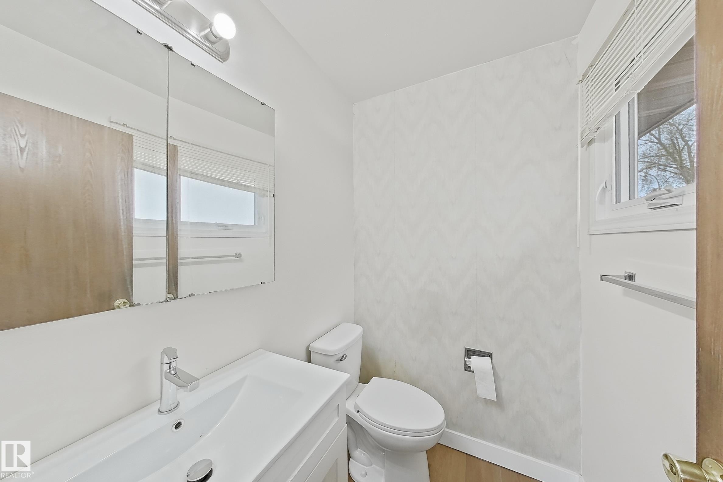 Bathroom featuring a white vanity with integrated sink, chrome faucet, wall-mounted medicine cabinet with integrated lighting, and a white toilet - 1731 51 Street, Edmonton, AB - Indoor Photo Showing Bathroom