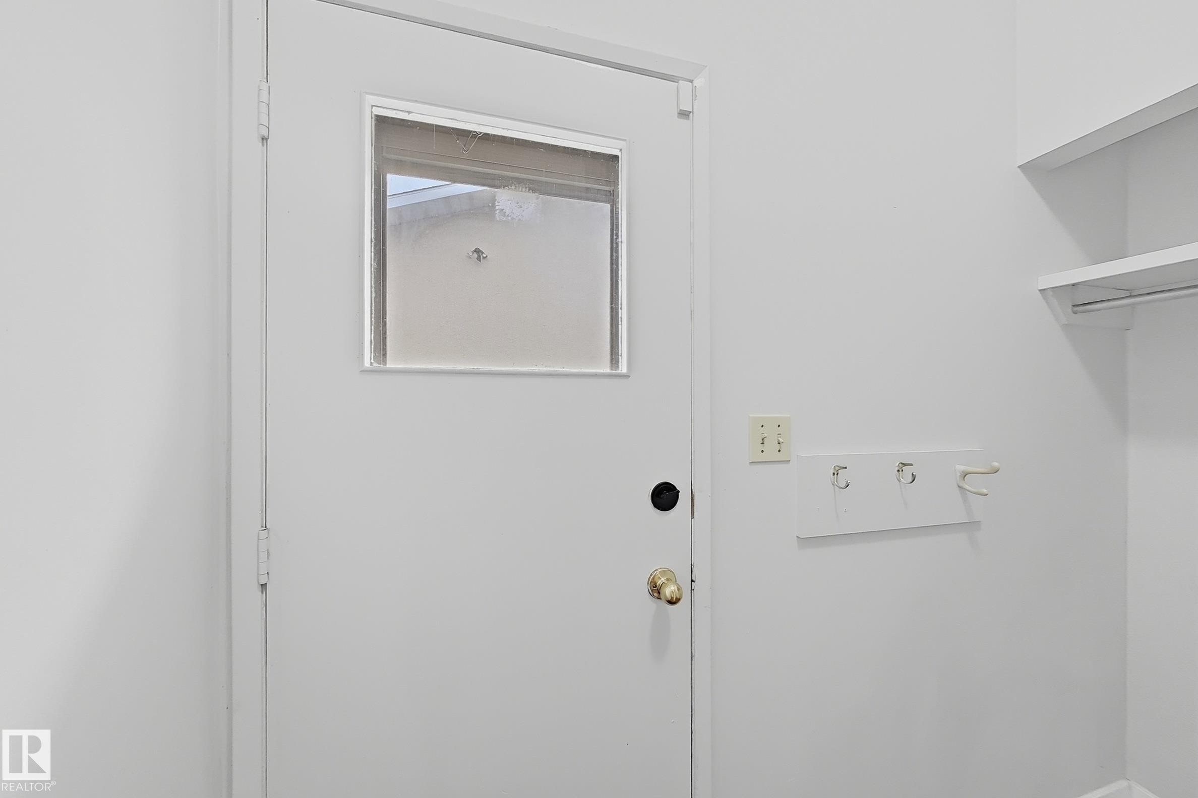White interior door with a pane of clear glass, brass-finish doorknob, and built-in shelving with hanging rod - 1731 51 Street, Edmonton, AB - Indoor Photo Showing Other Room
