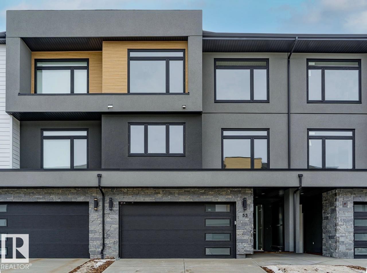 Contemporary multi-story exterior featuring a grey stucco facade, black-framed windows, and stone veneer accents - 53 7121 May Crescent, Edmonton, AB - Outdoor