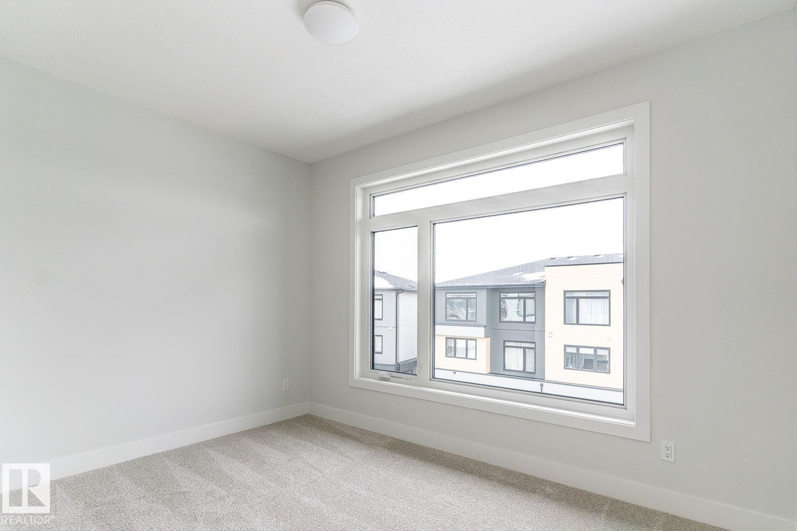 Bright interior space featuring a large picture window, neutral wall paint, and light-colored carpeting - 53 7121 May Crescent, Edmonton, AB - Indoor Photo Showing Other Room