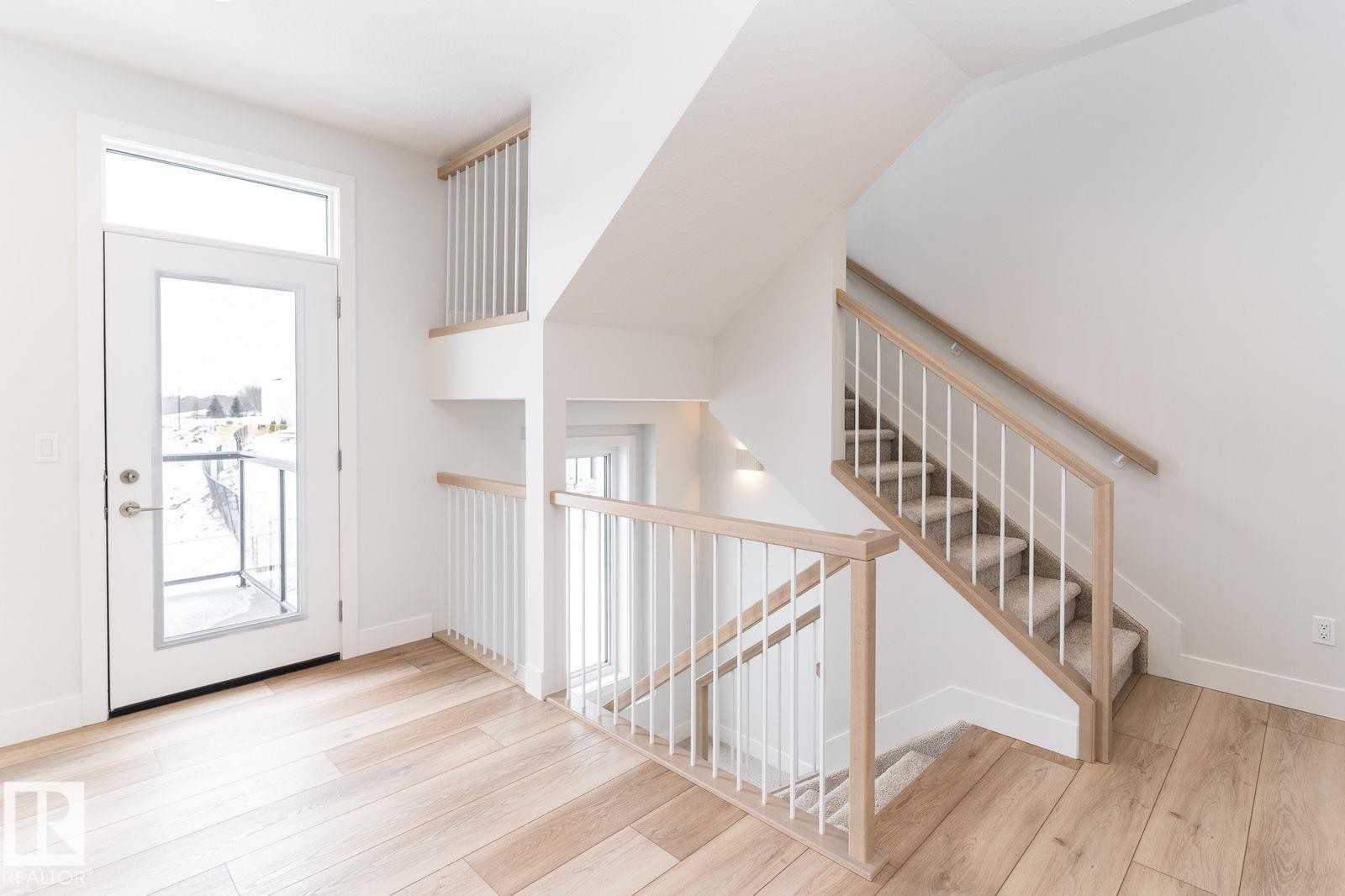 Multilevel interior featuring light wood-finish flooring, white walls, and a contemporary staircase with light wood handrails and white balusters - 53 7121 May Crescent, Edmonton, AB - Indoor Photo Showing Other Room