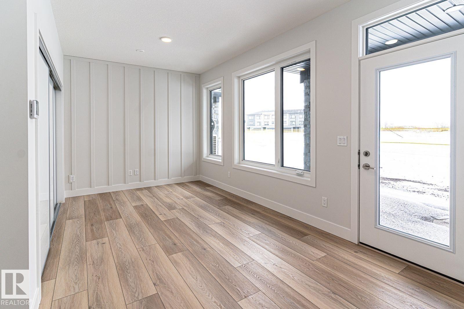Spacious room featuring wide plank wood-finish flooring, a contemporary board and batten accent wall, and recessed lighting - 53 7121 May Crescent, Edmonton, AB - Indoor Photo Showing Other Room