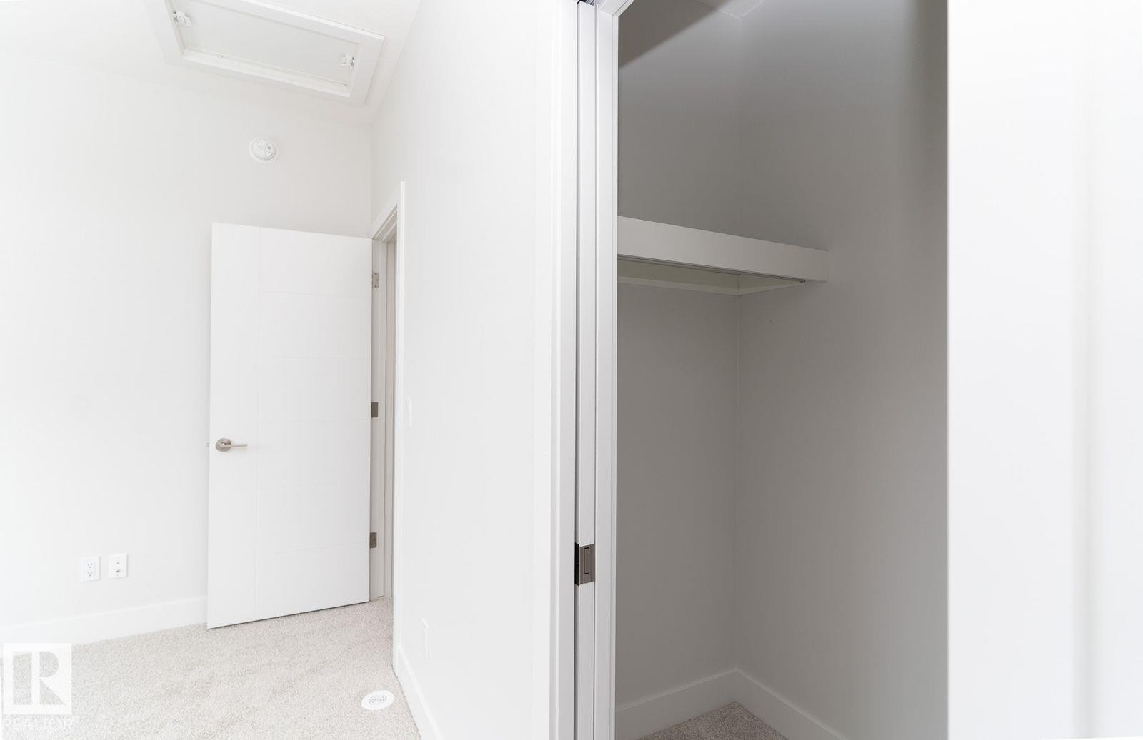 Clean white interior featuring light-toned carpet, a contemporary interior door with brushed nickel hardware, and a closet with integrated shelving and hanging rod - 53 7121 May Crescent, Edmonton, AB - Indoor Photo Showing Other Room