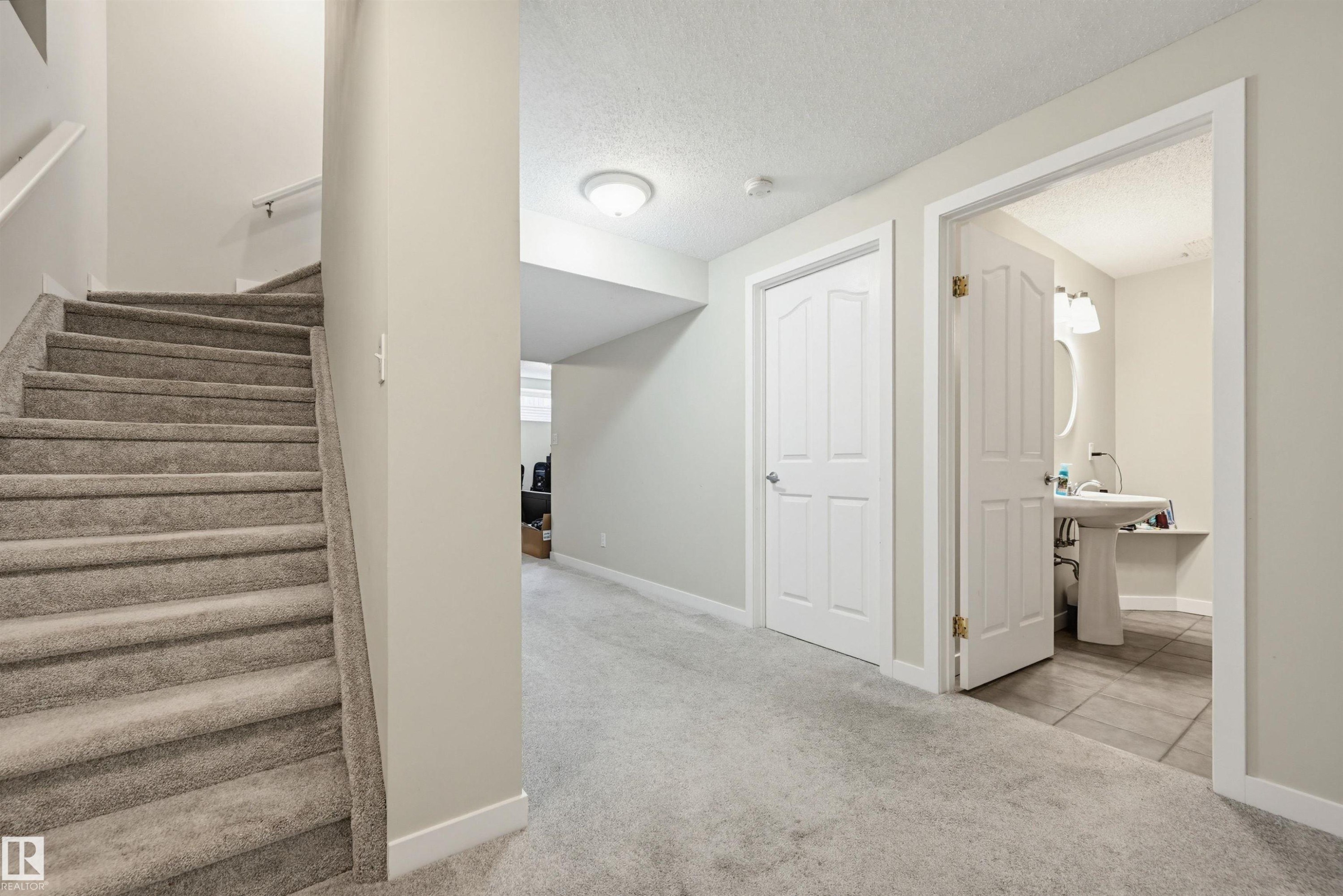 Carpeted staircase with a white handrail, leading to a hallway with light gray walls and recessed lighting - 11 3380 28A Avenue Nw, Edmonton, AB - Indoor