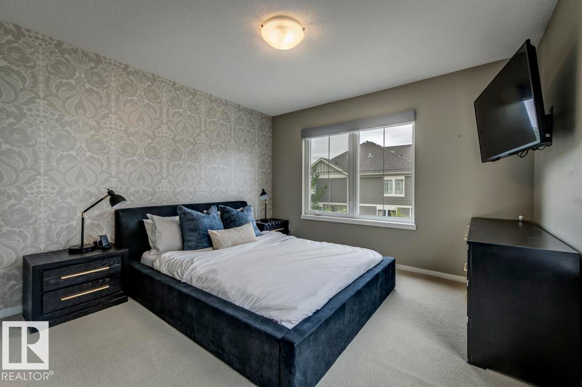 Interior room featuring a patterned accent wall, neutral wall paint, and a double-pane window with a roller shade - 67 603 Watt Boulevard, Edmonton, AB - Indoor Photo Showing Bedroom
