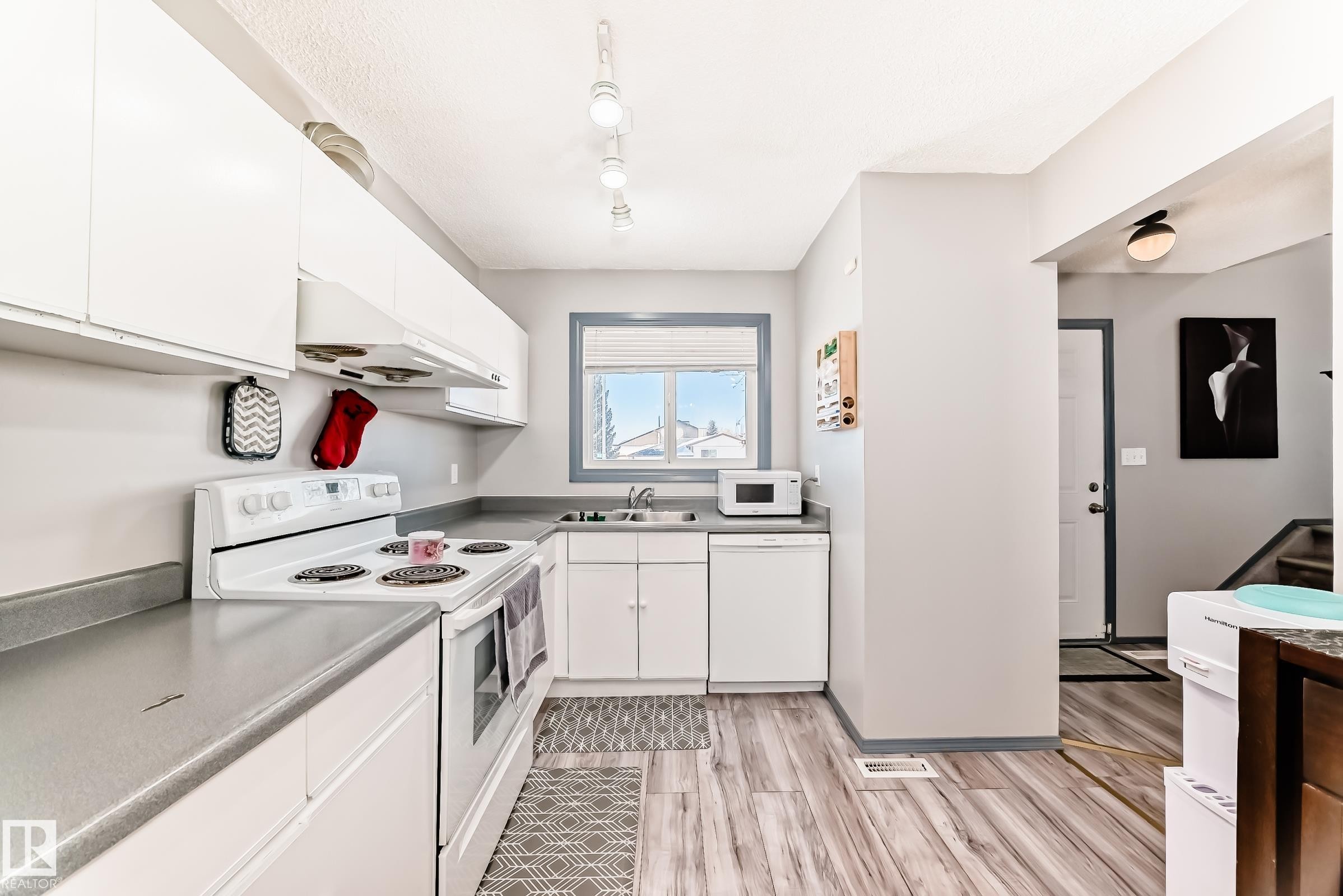 Kitchen featuring white cabinetry and appliances, grey countertops, wood-finish flooring, and a window with blue trim - 214A Warwick Road, Edmonton, AB - Indoor Photo Showing Kitchen With Double Sink
