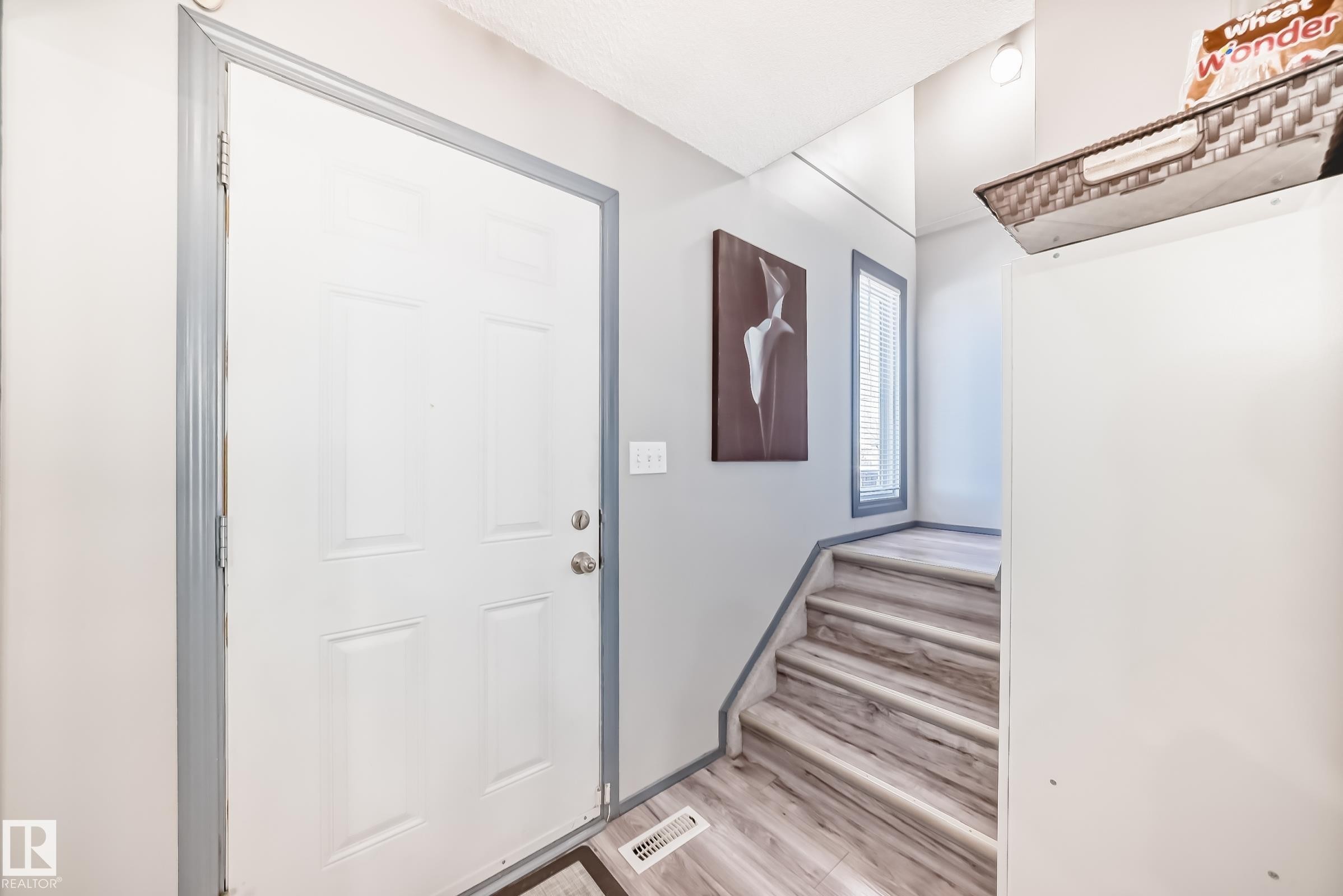 Entryway featuring a paneled door with light grey trim, wood-finish flooring, and a multi-level staircase with matching wood-finish treads - 214A Warwick Road, Edmonton, AB - Indoor Photo Showing Other Room
