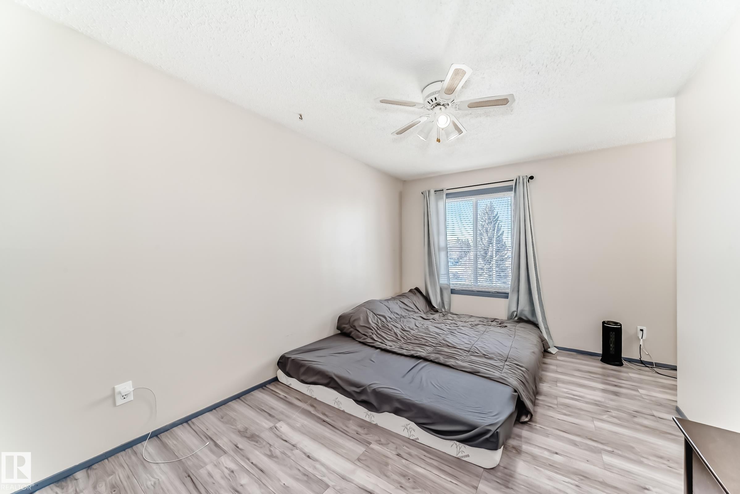 Room featuring wood-finish flooring, a window with curtains, and a ceiling fan with integrated lighting - 214A Warwick Road, Edmonton, AB - Indoor Photo Showing Bedroom