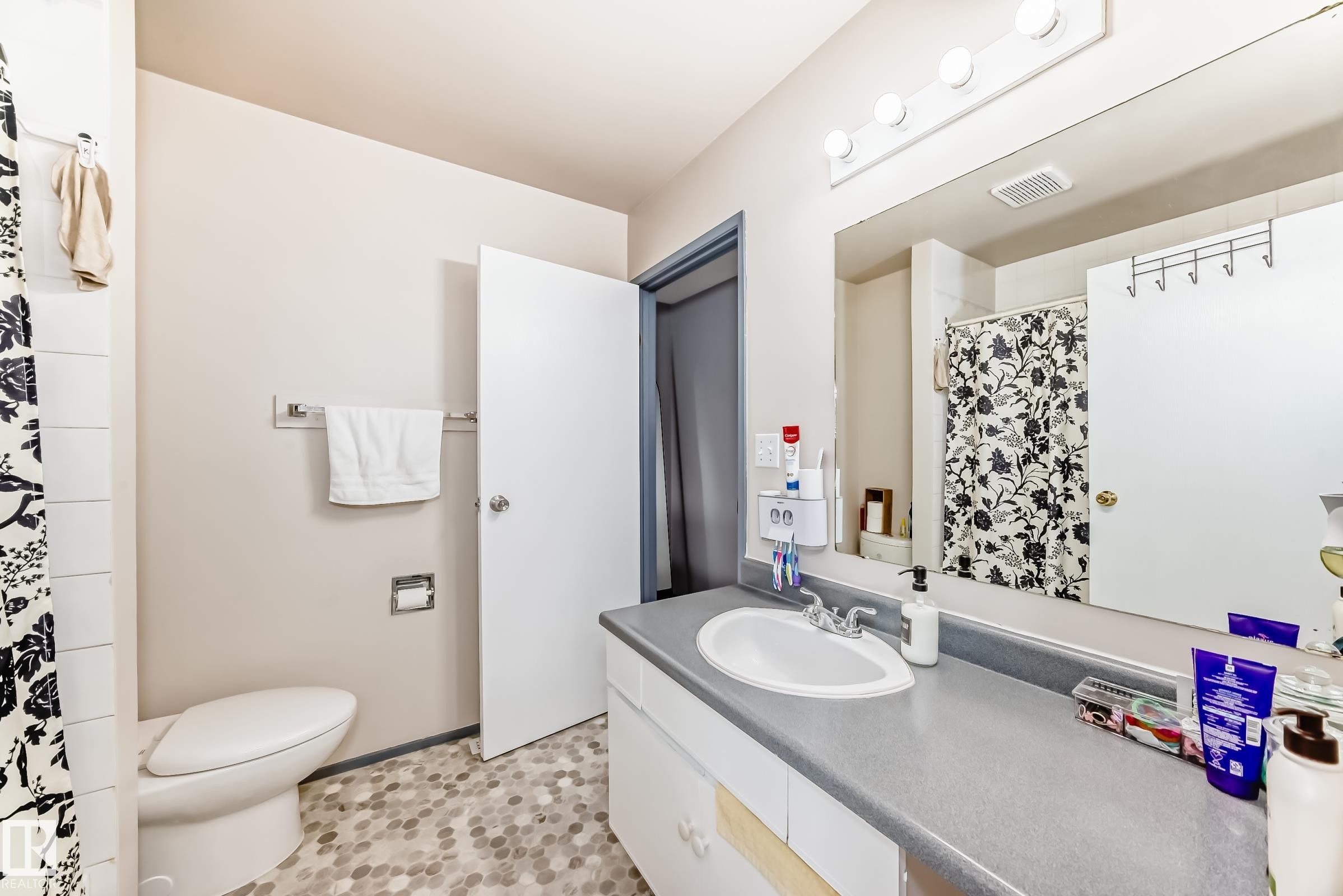 Bathroom featuring a vanity with an integrated sink, a large wall-mounted mirror, overhead vanity lighting, and mosaic tile flooring - 214A Warwick Road, Edmonton, AB - Indoor Photo Showing Bathroom