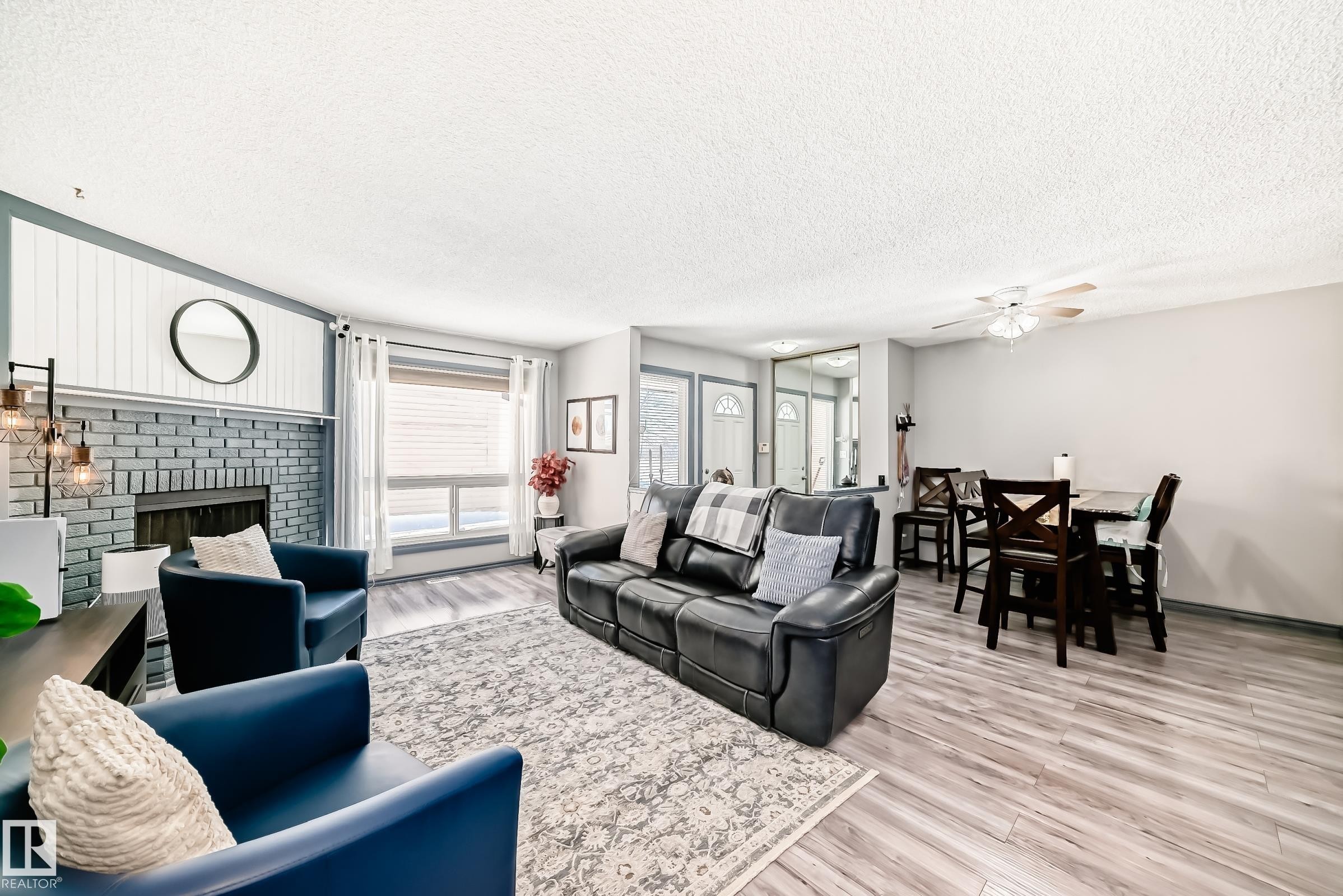 Spacious living area featuring a painted brick fireplace with a shiplap accent wall, wood-finish flooring, and large windows - 214A Warwick Road, Edmonton, AB - Indoor Photo Showing Living Room With Fireplace