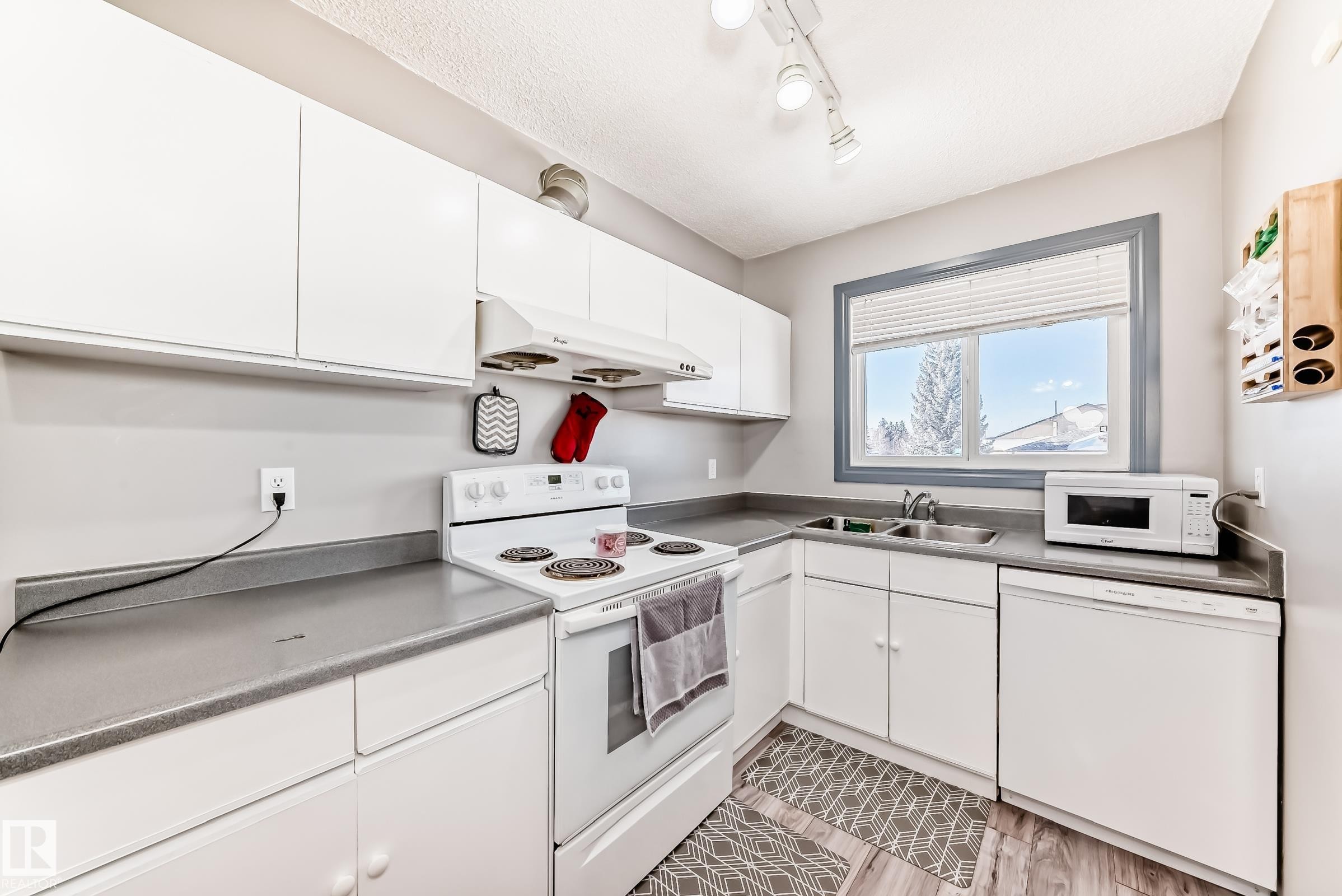 Kitchen featuring white cabinetry, grey countertops, white appliances, and wood-finish flooring - 214A Warwick Road, Edmonton, AB - Indoor Photo Showing Kitchen With Double Sink