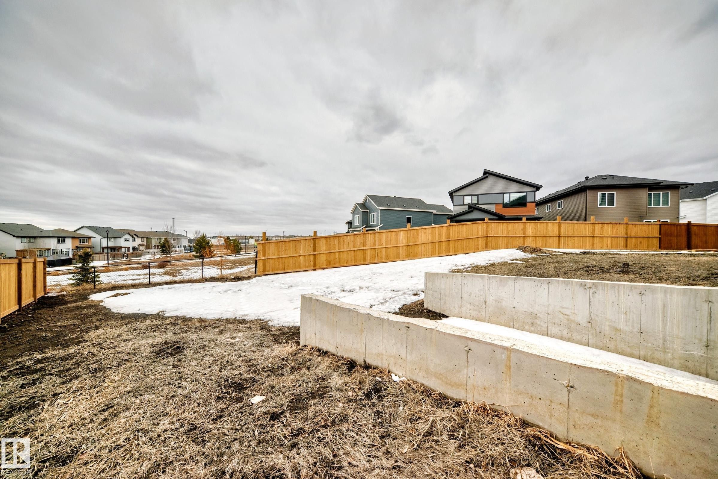 The property features a tiered concrete retaining wall and a wooden fence - 4509 170A Avenue, Edmonton, AB - Outdoor