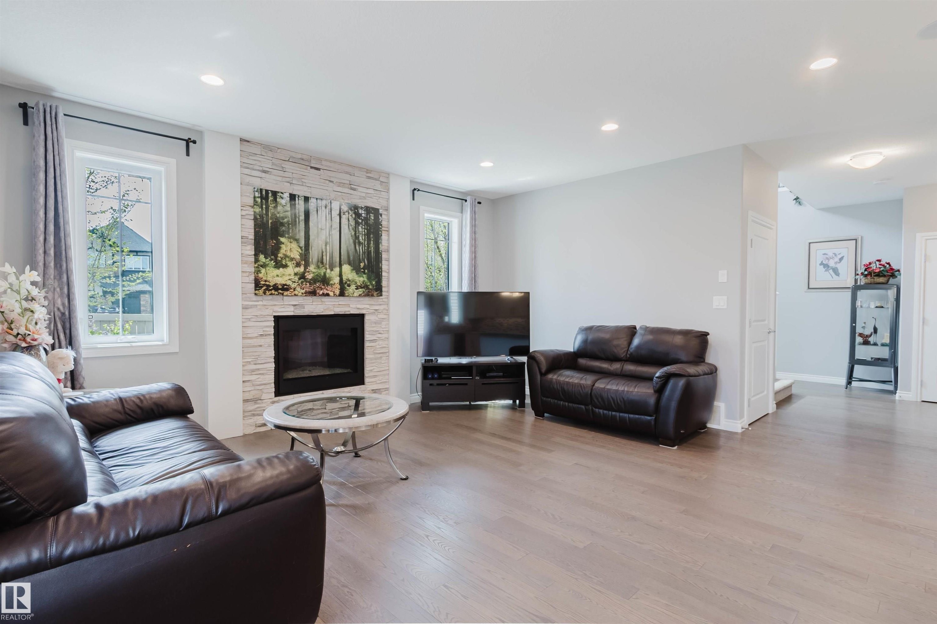 Spacious living area featuring light wood-finish flooring, a contemporary fireplace with a stacked stone facade, and recessed ceiling lighting - 3571 Keswick Boulevard, Edmonton, AB - Indoor Photo Showing Living Room With Fireplace
