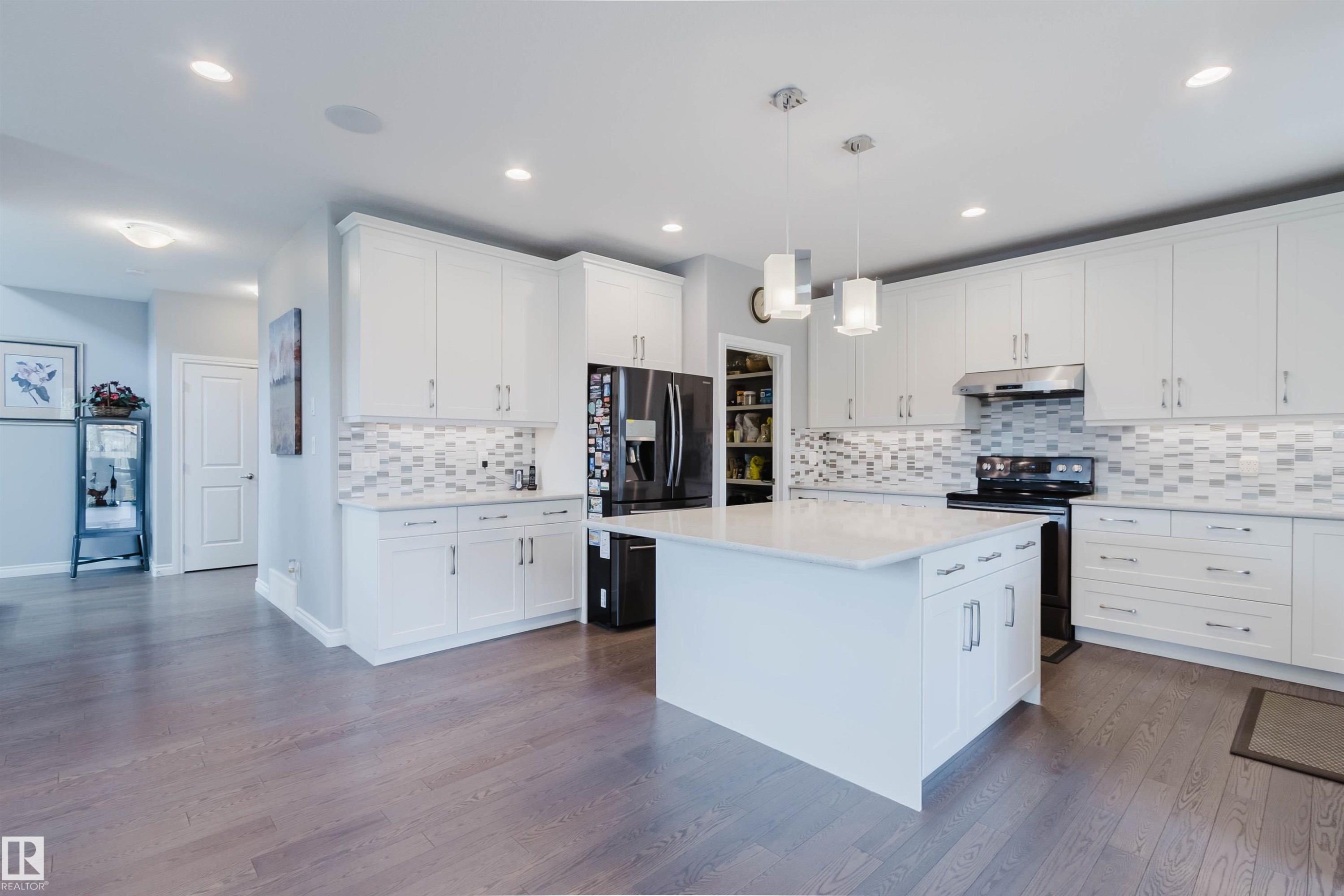 Modern kitchen featuring white shaker cabinetry, an expansive center island with a stone countertop, a tile backsplash, stainless steel appliances, and recessed lighting - 3571 Keswick Boulevard, Edmonton, AB - Indoor Photo Showing Kitchen With Upgraded Kitchen