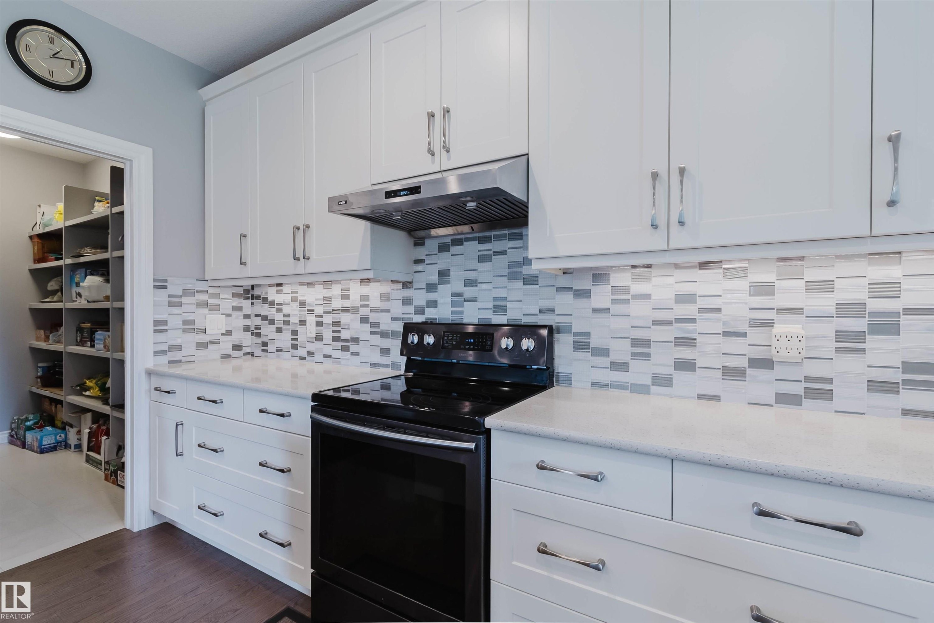 White shaker-style cabinetry with chrome hardware, a patterned tile backsplash, and a built-in stainless steel range hood - 3571 Keswick Boulevard, Edmonton, AB - Indoor Photo Showing Kitchen