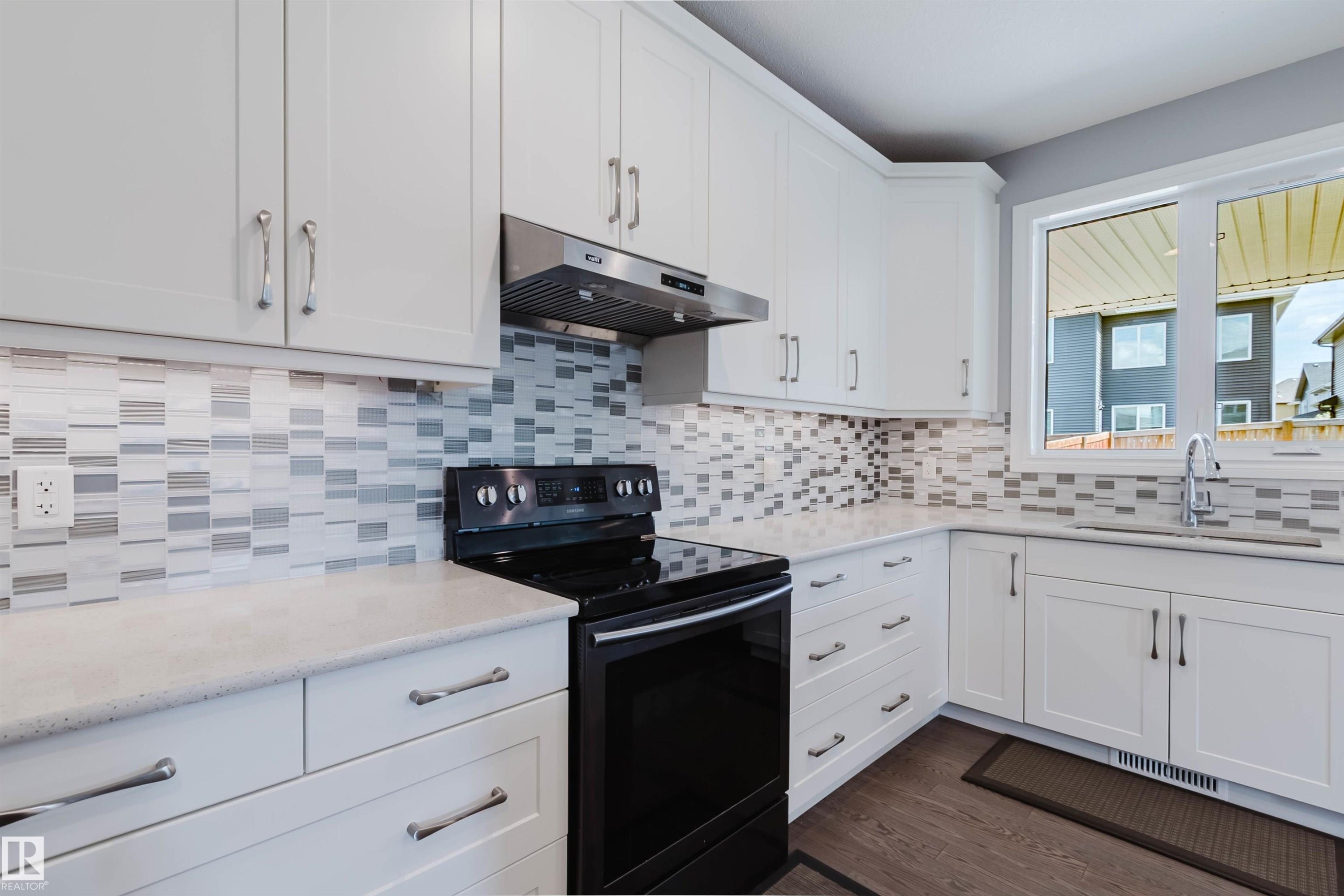 Modern kitchen featuring white shaker cabinetry, light-toned countertops, and a full tile backsplash with a mosaic pattern - 3571 Keswick Boulevard, Edmonton, AB - Indoor Photo Showing Kitchen