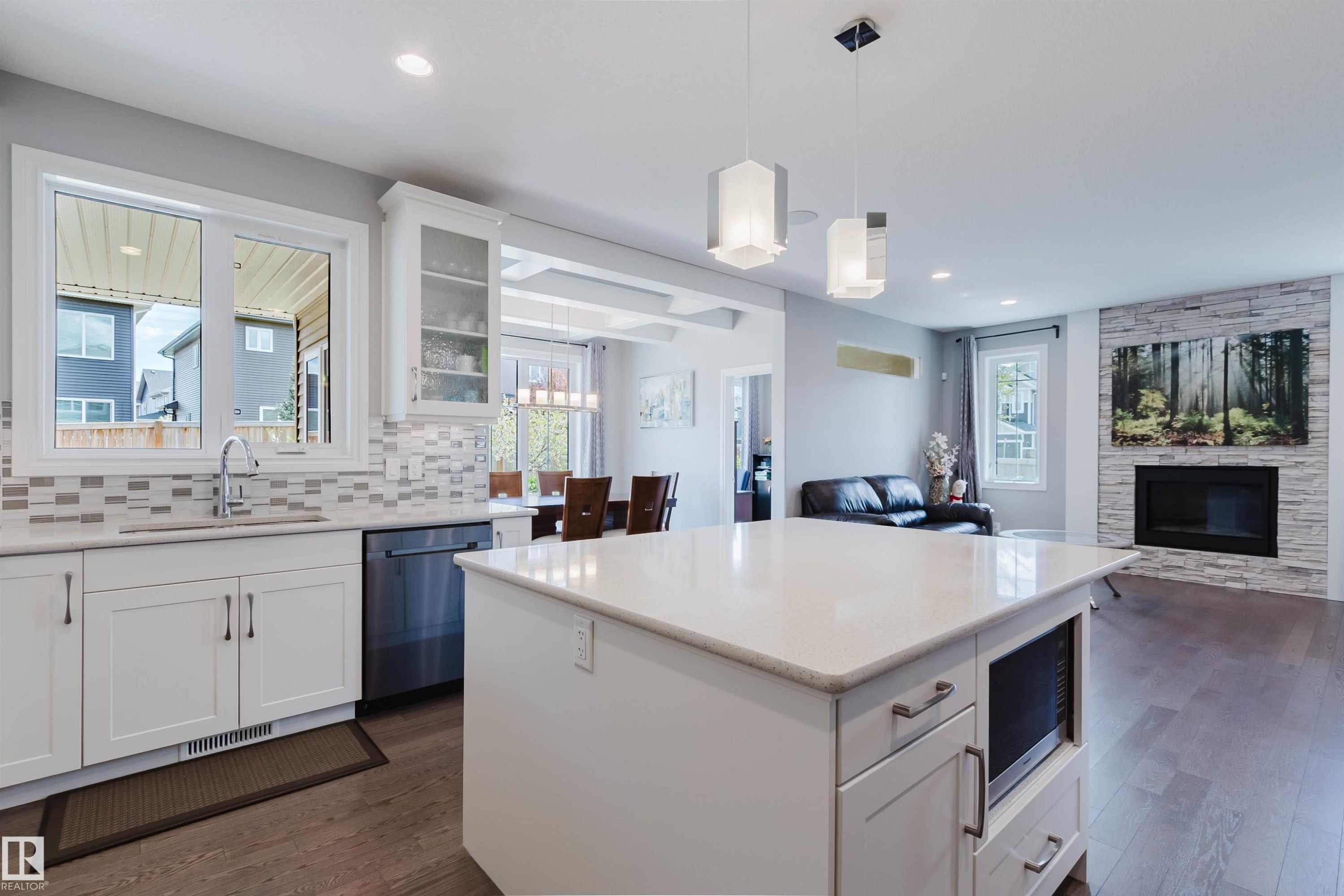 Open-concept kitchen featuring a large island with integrated microwave, white cabinetry, a tile backsplash, and stainless steel appliances - 3571 Keswick Boulevard, Edmonton, AB - Indoor Photo Showing Kitchen