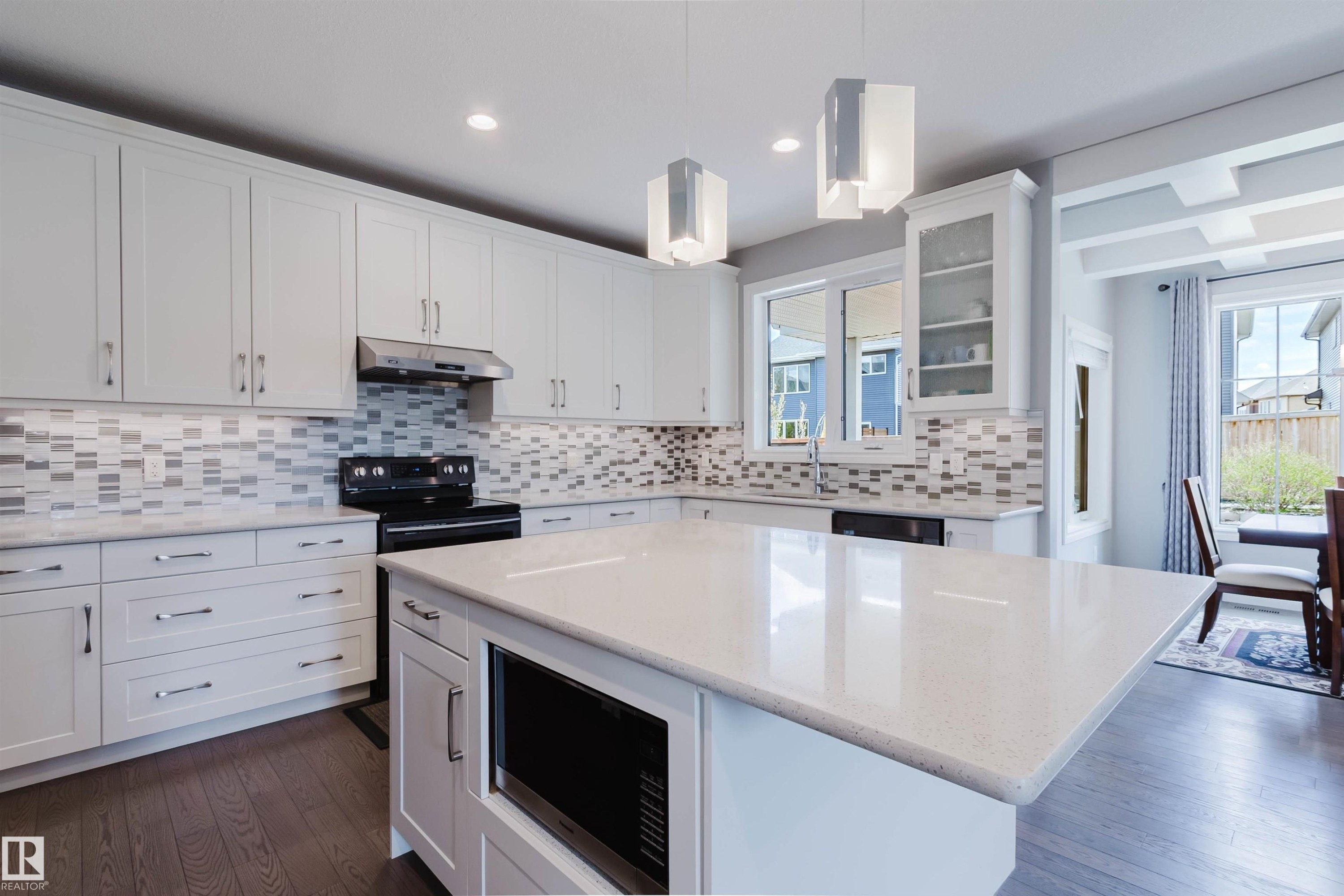 Kitchen featuring a large central island with a built-in microwave, white shaker-style cabinetry, mosaic tile backsplash, and wood-finish flooring - 3571 Keswick Boulevard, Edmonton, AB - Indoor Photo Showing Kitchen With Upgraded Kitchen