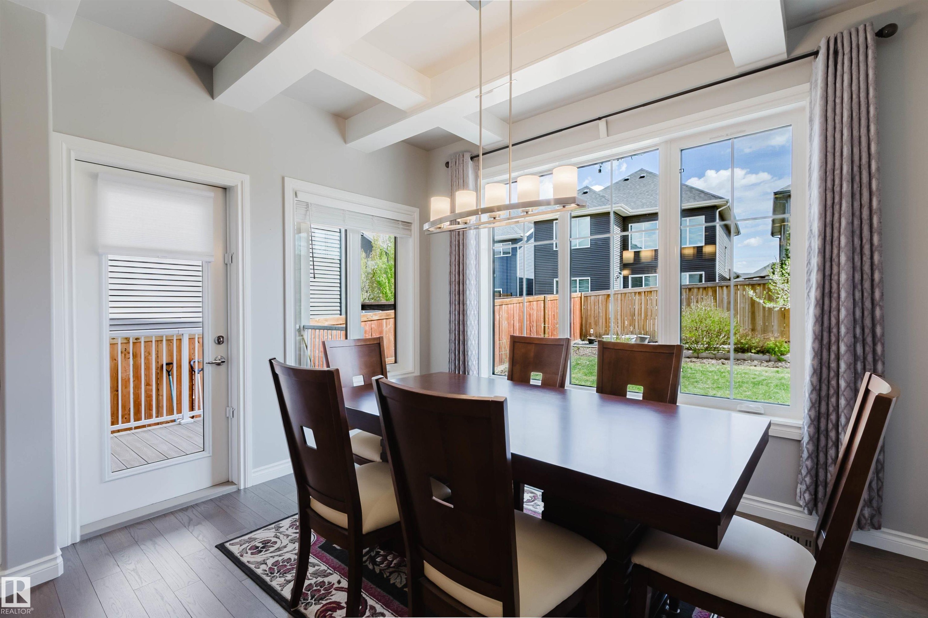 Dining area featuring coffered ceilings, contemporary linear chandelier, wood-finish flooring, and ample natural light from large windows - 3571 Keswick Boulevard, Edmonton, AB - Indoor Photo Showing Other Room