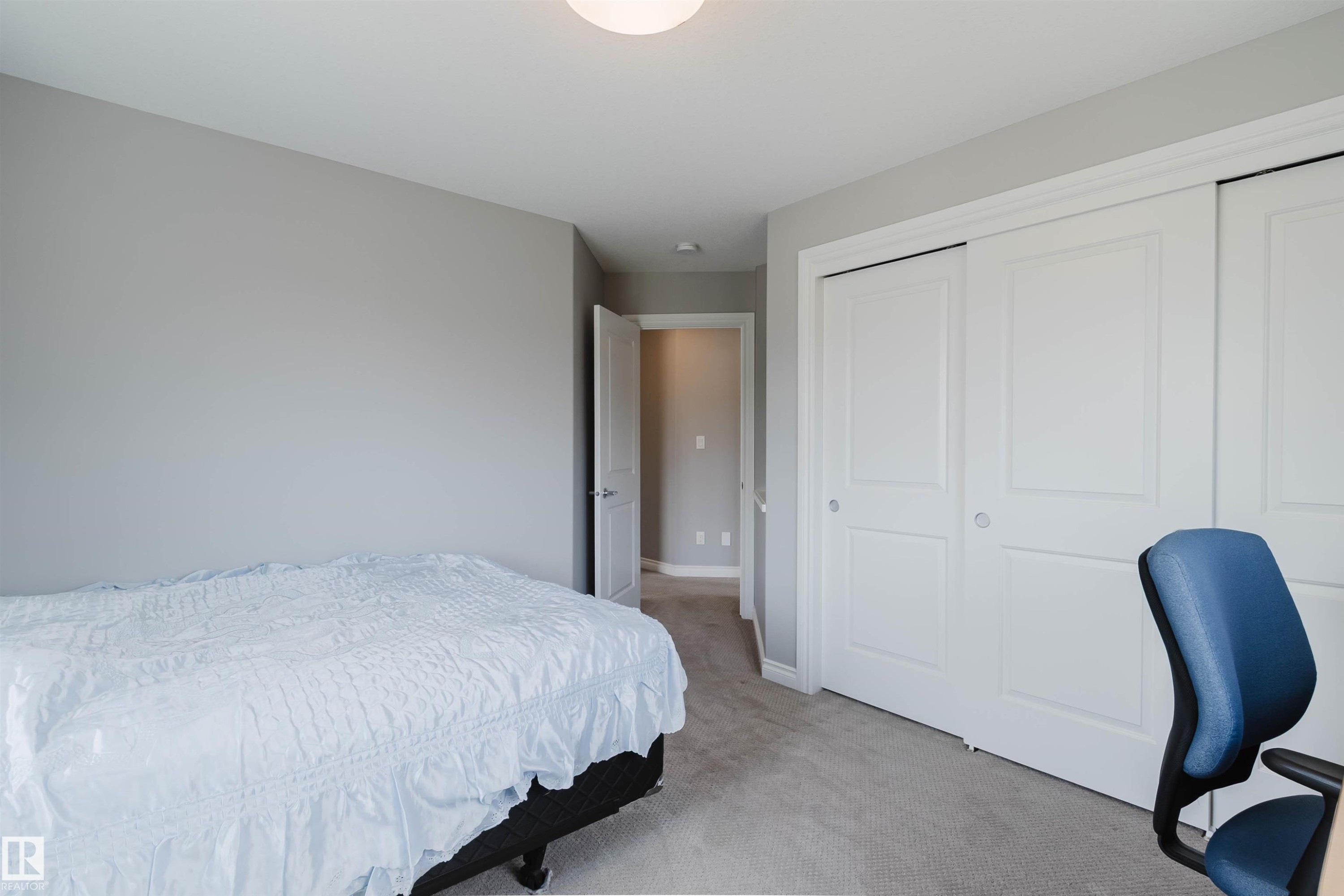 Carpeted room with a double-panel closet featuring sliding doors, neutral wall paint, white trim, and a flush-mount ceiling light - 3571 Keswick Boulevard, Edmonton, AB - Indoor Photo Showing Bedroom
