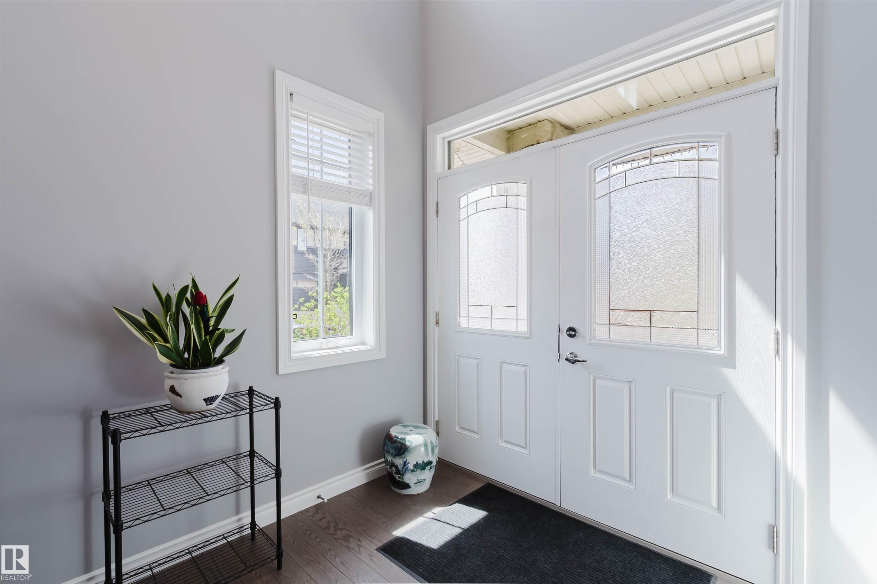 Double entry doors featuring decorative glass inserts and a transom window, complemented by wood-finish flooring and a single-pane window with white blinds - 3571 Keswick Boulevard, Edmonton, AB - Indoor Photo Showing Other Room