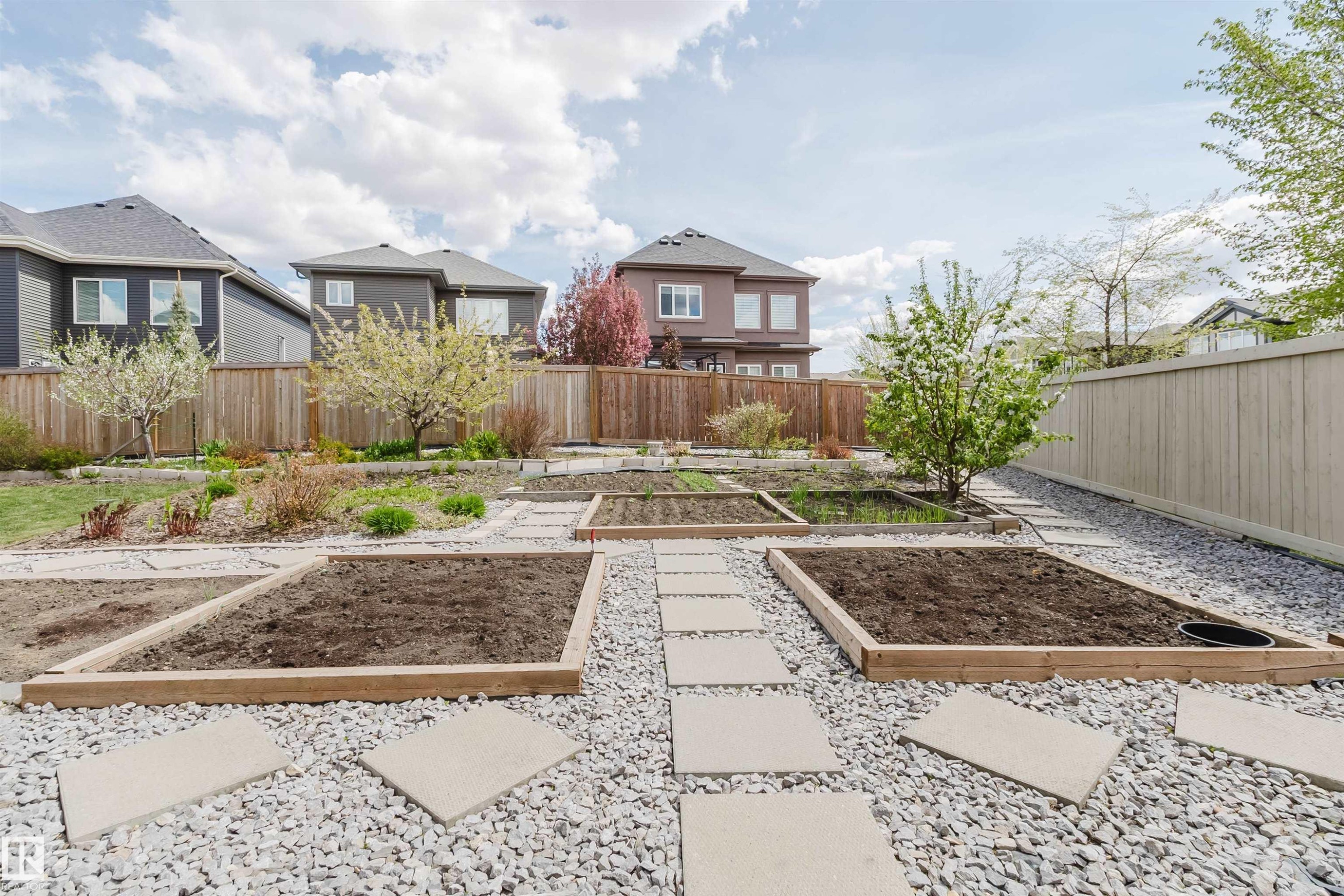 Rear yard featuring multiple raised garden beds, gravel pathways, square stepping stones, and mature trees - 3571 Keswick Boulevard, Edmonton, AB - Outdoor