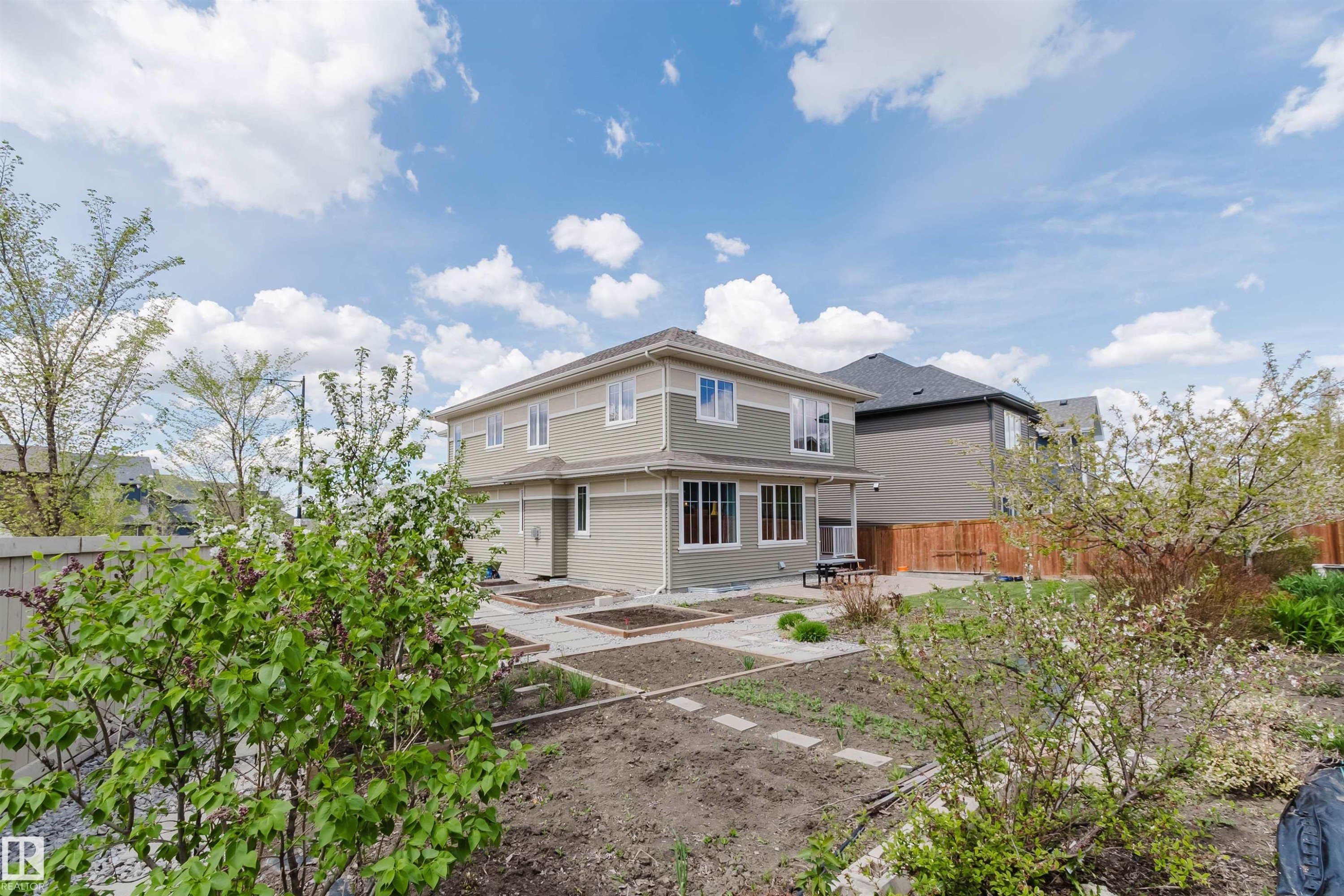 Multi-level exterior with light green and beige siding, featuring multiple windows, a ground-level patio, and a covered porch area - 3571 Keswick Boulevard, Edmonton, AB - Outdoor