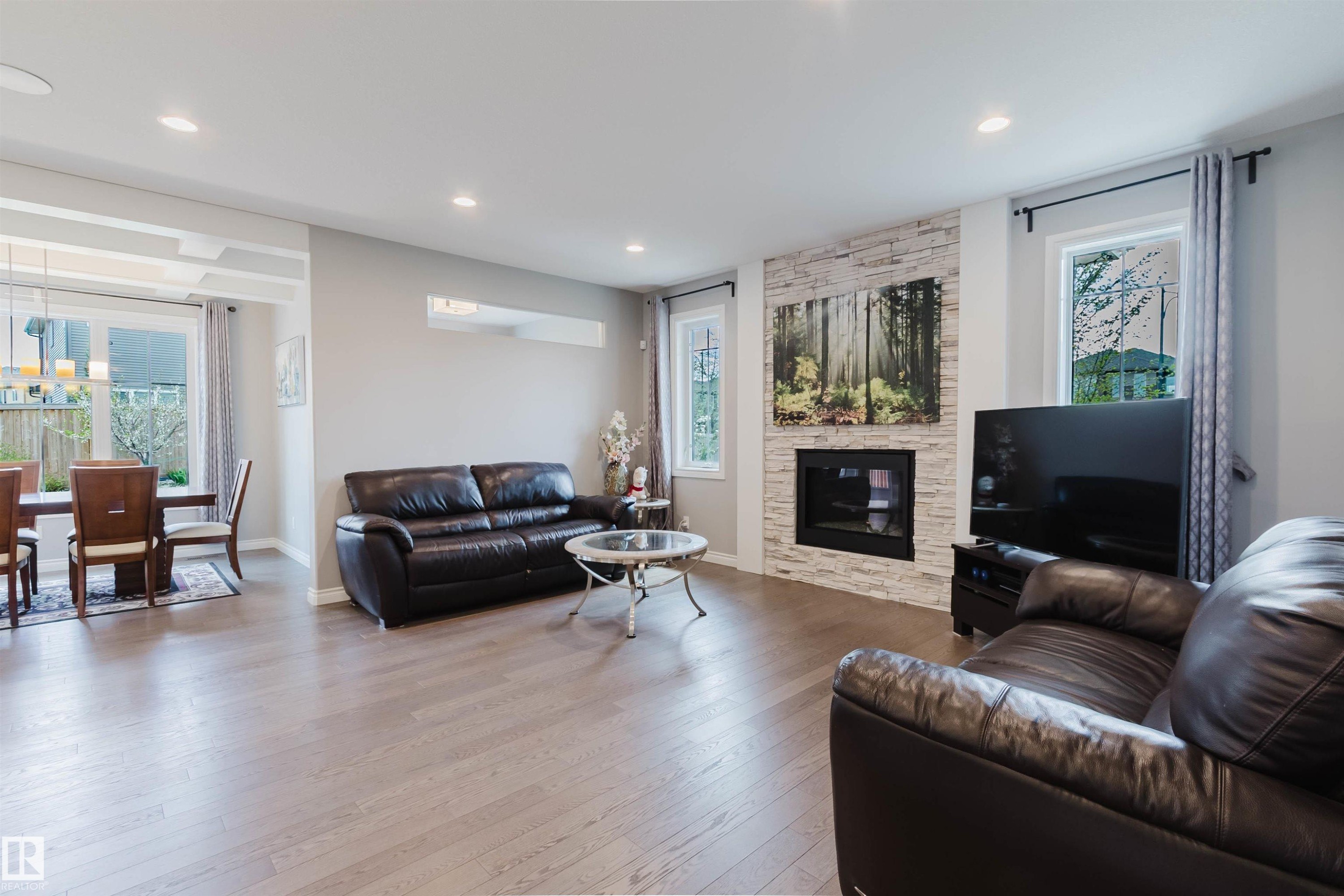 Spacious living area featuring wood-finish flooring, recessed lighting, and a stone-clad fireplace - 3571 Keswick Boulevard, Edmonton, AB - Indoor Photo Showing Living Room With Fireplace